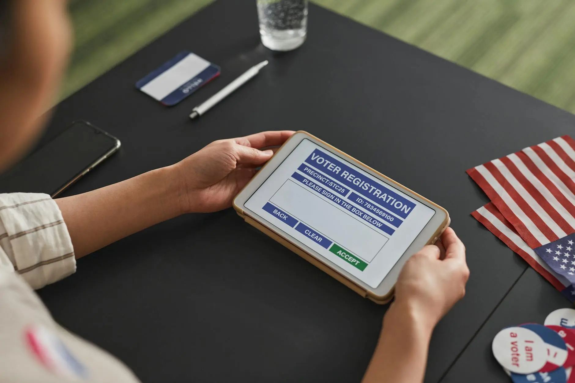 A person using a tablet showing a voter registration interface on a black table.