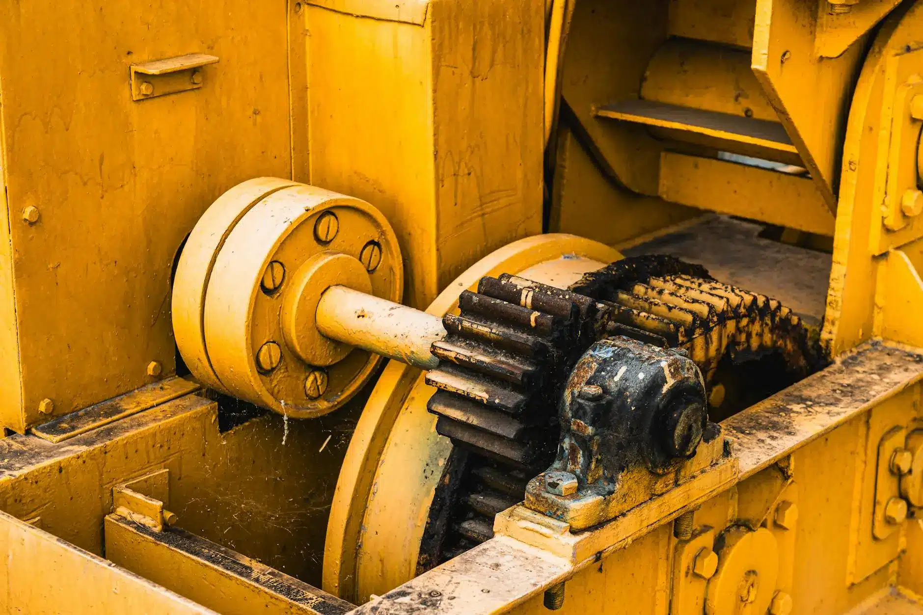Close-up of yellow machinery with gears and pulleys showing signs of wear and dust.