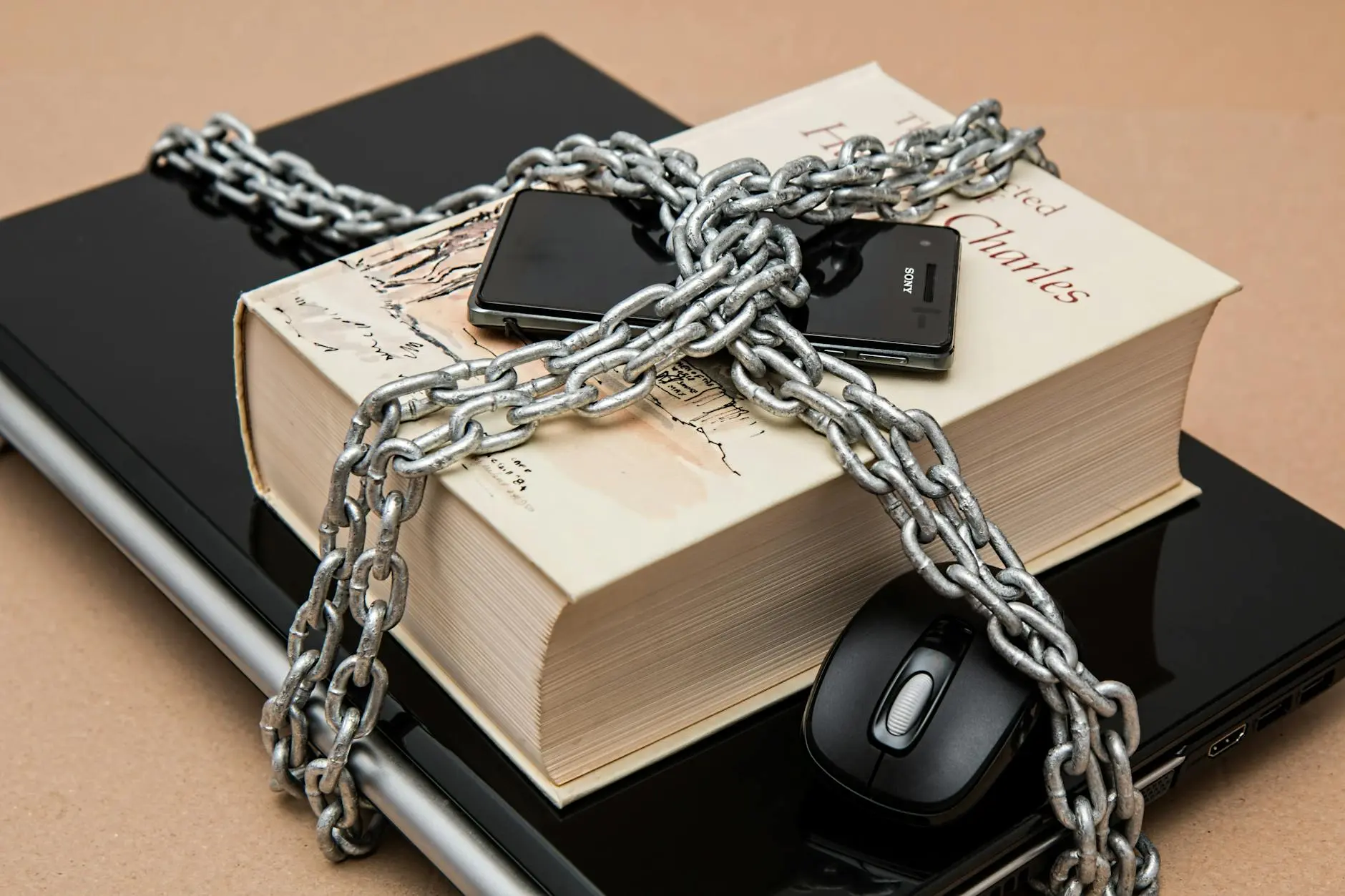 A book chained with a smartphone and computer mouse on a black laptop surface.