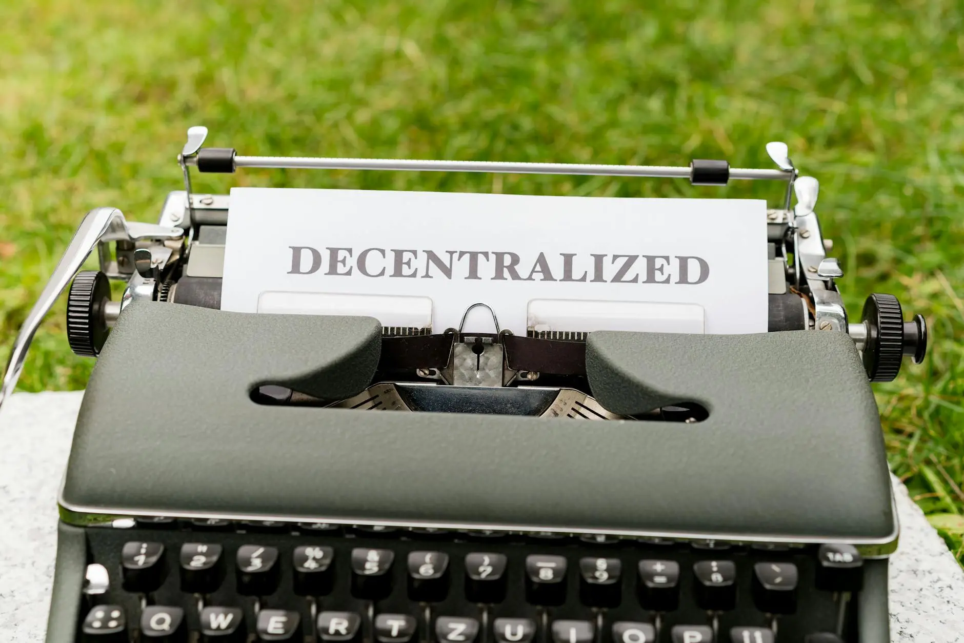 Typewriter with a sheet of paper that reads 'DECENTRALIZED' against a grassy background.