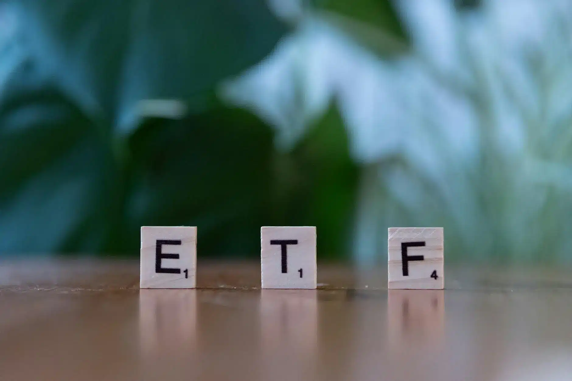 Three wooden letter tiles spelling 'ETF' on a wooden surface with a blurred green background.