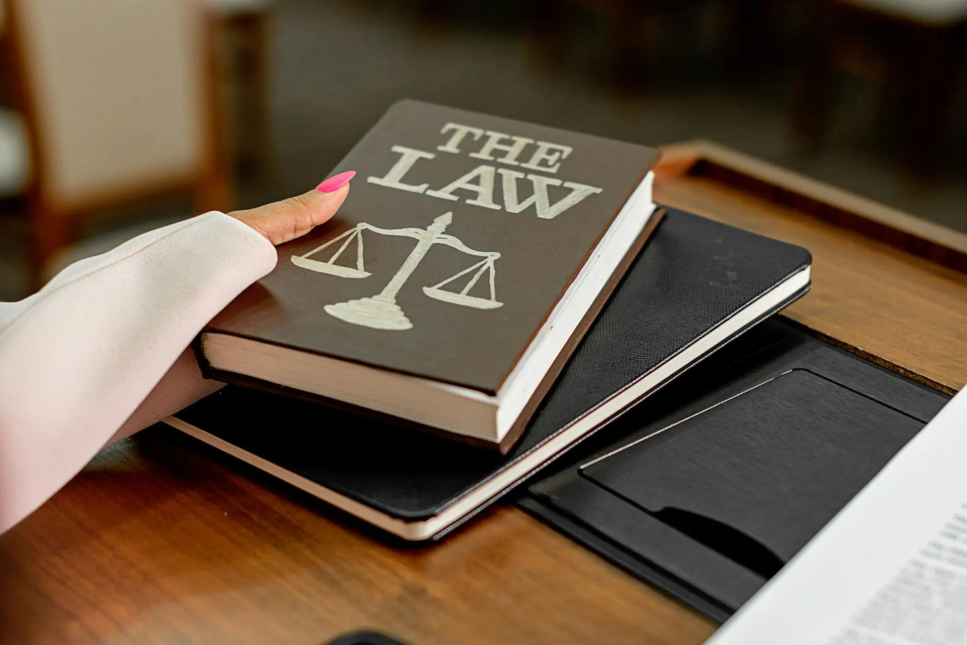 A hand lightly holding a book titled 'THE LAW' on a desk with two notebooks.