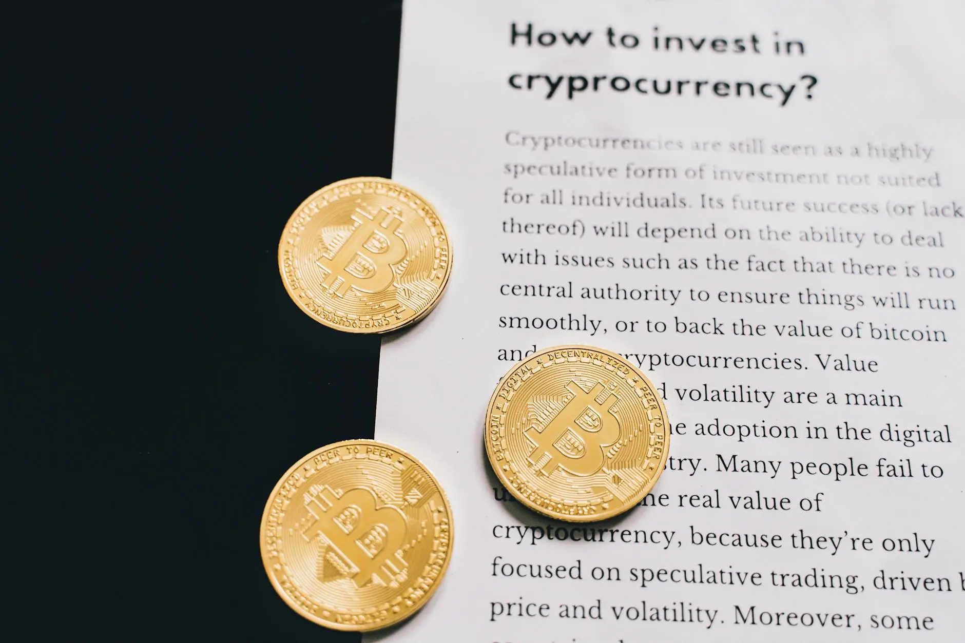 Three gold Bitcoin coins placed on a dark surface next to a printed article about cryptocurrency investment.