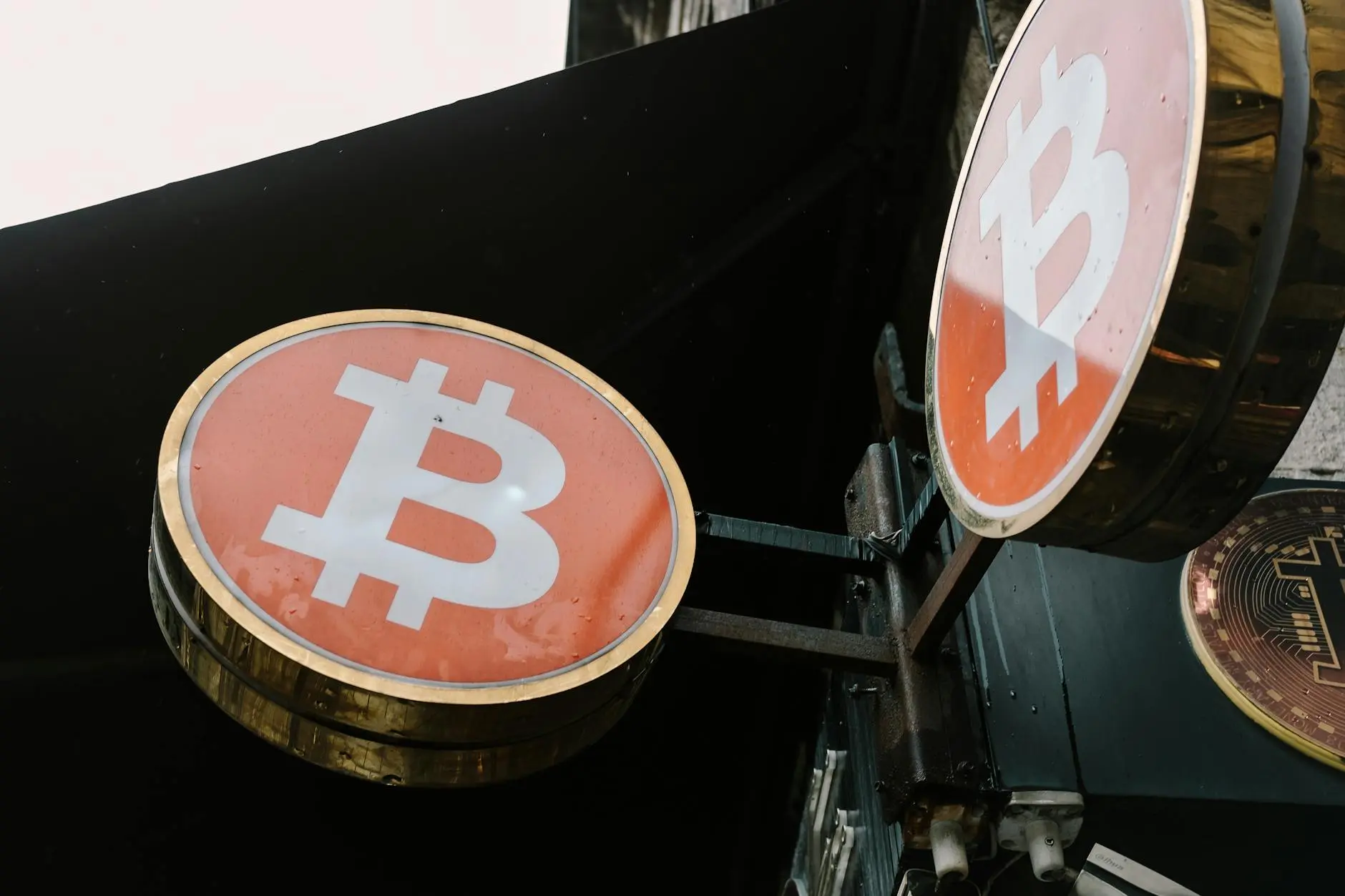 Two illuminated Bitcoin signs hanging on a wall with a dark background.