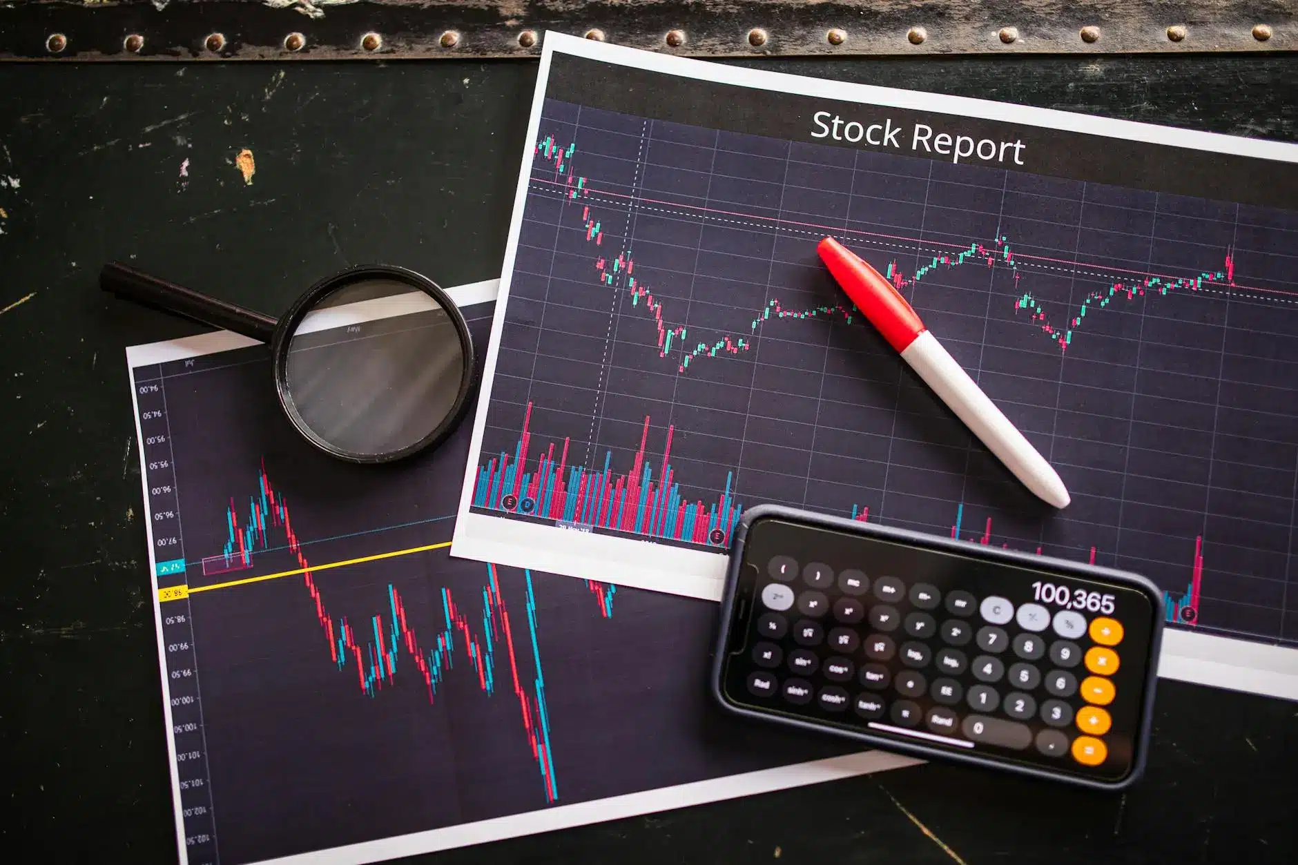 A stock report with charts, a magnifying glass, and a calculator on a dark surface.