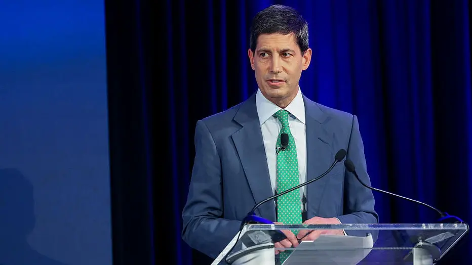 A man in a blue suit and green tie speaks at a podium with a microphone.