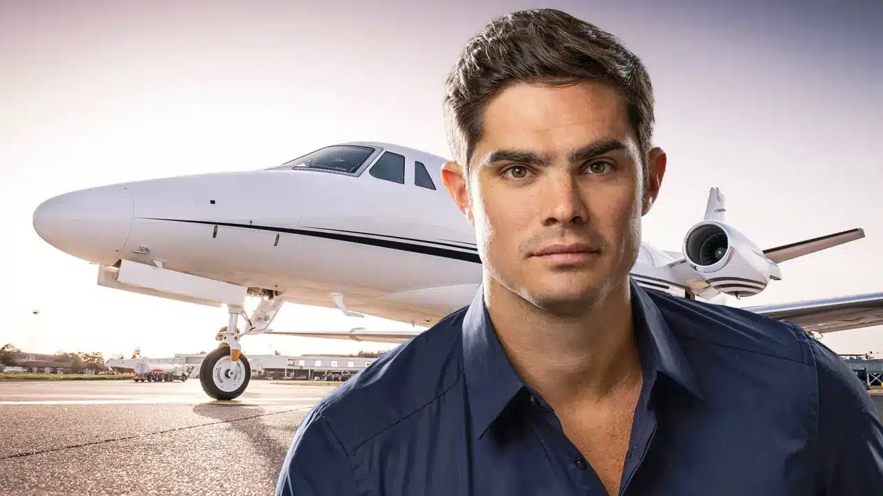 A man in a blue shirt stands in front of a private jet on an airport tarmac.