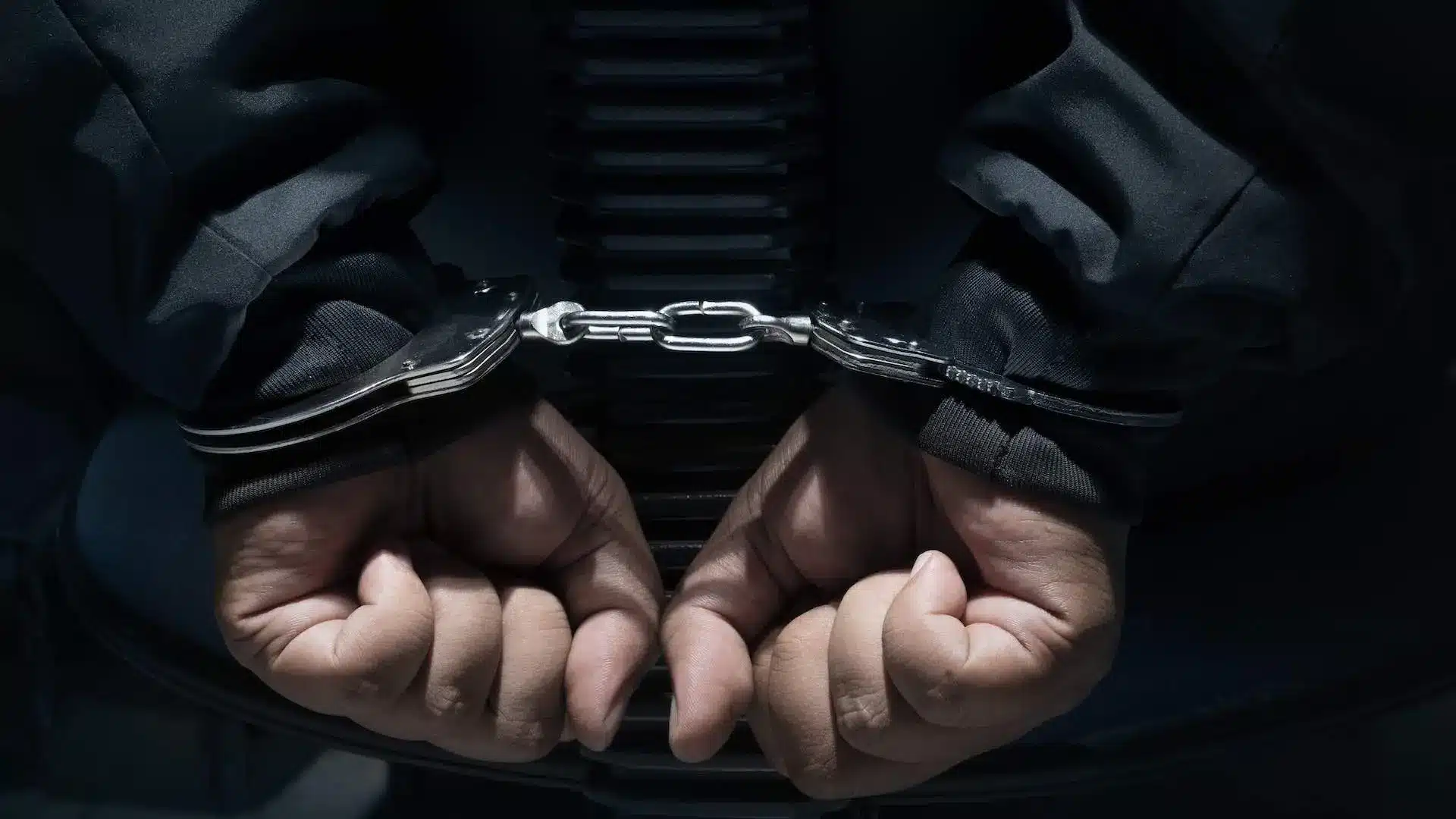 Close-up of hands in handcuffs against a dark background.