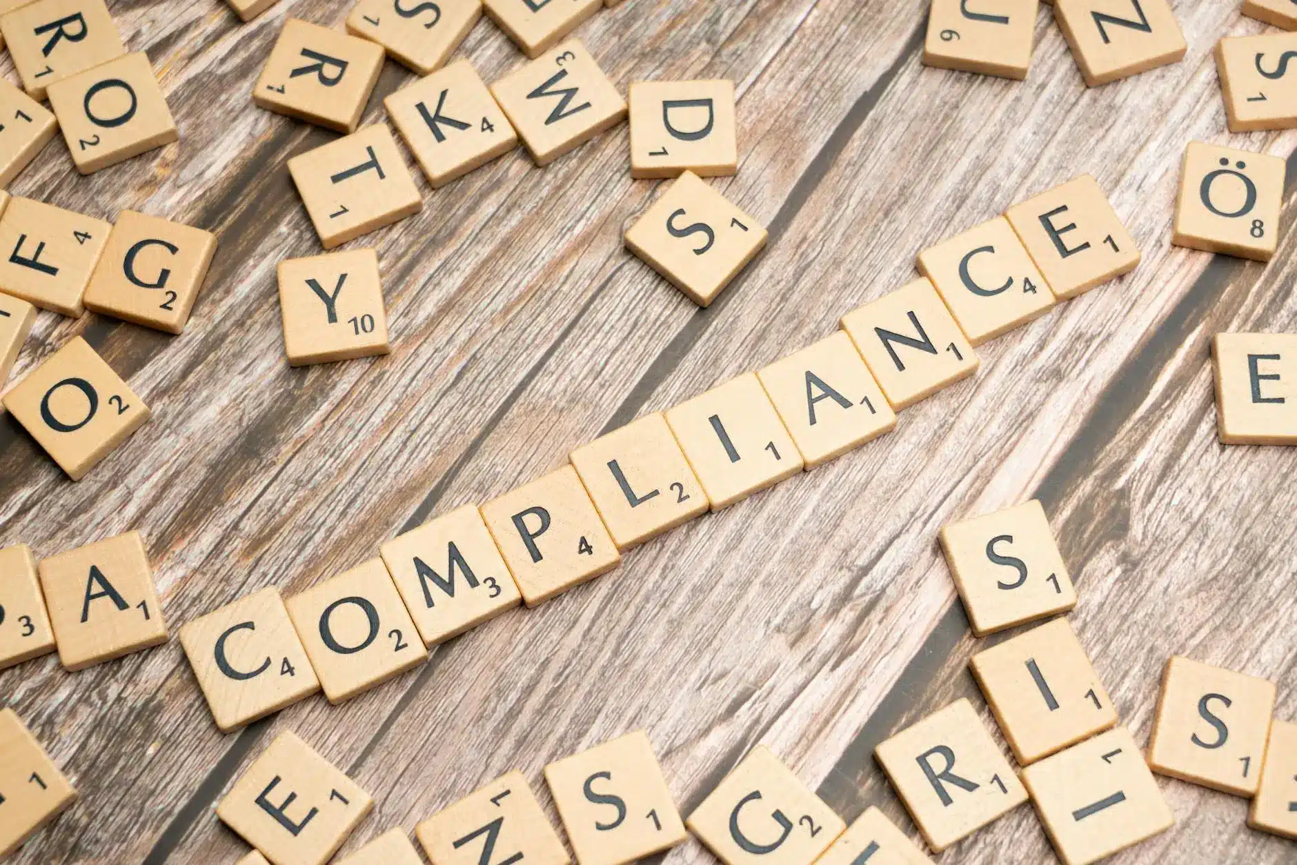 Scrabble tiles arranged on a wooden surface spell out 'COMPLIANCE'.