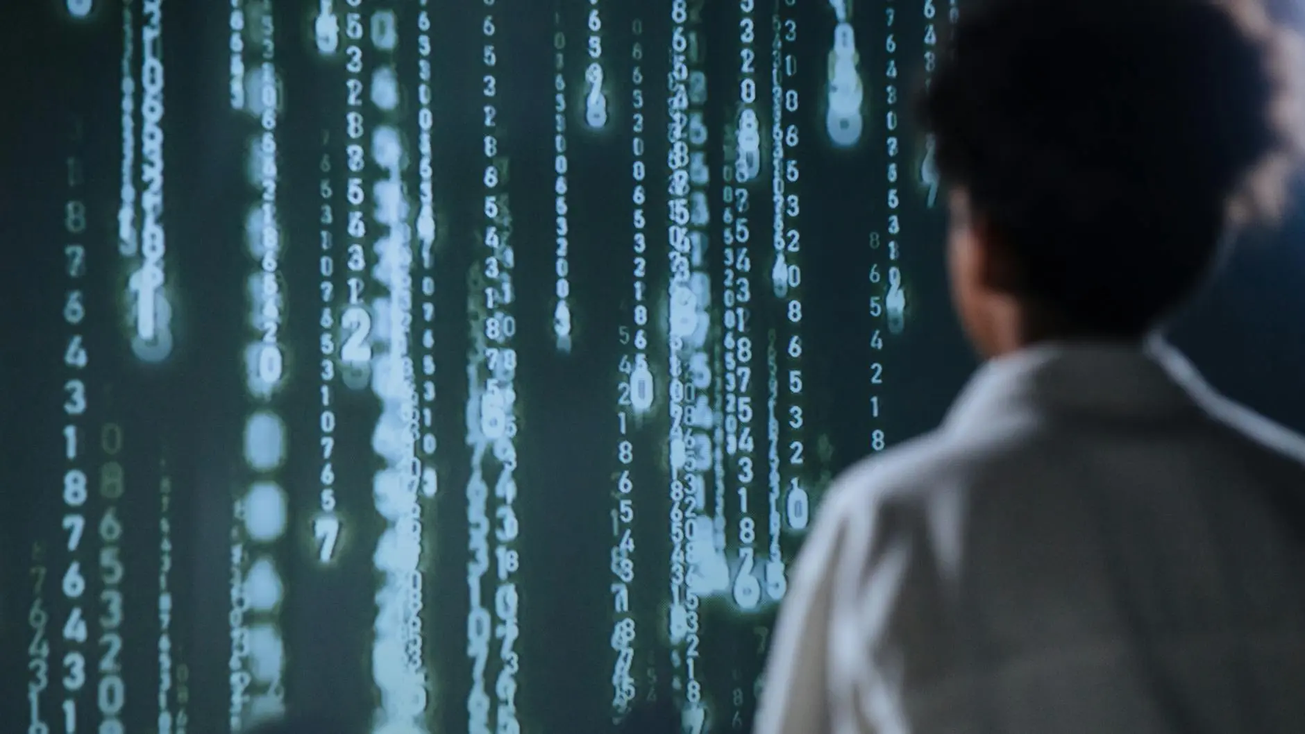 Person viewing cascading binary numbers on a screen, symbolizing data processing.