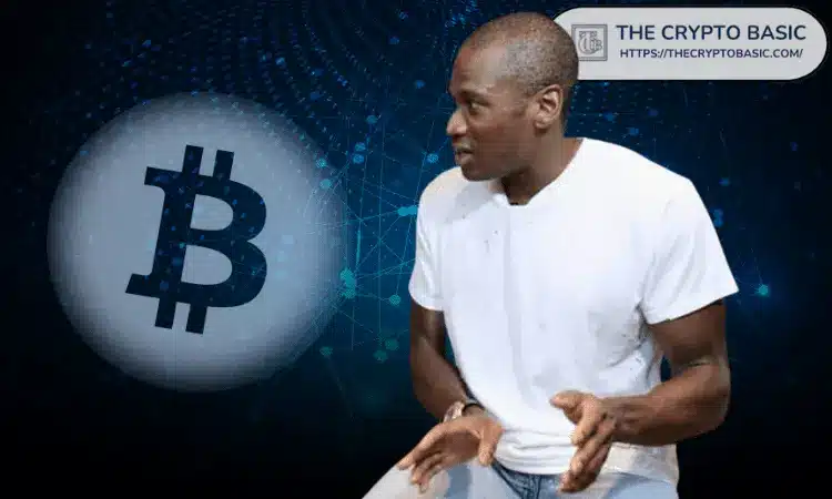 A man in a white shirt gestures as he speaks, with a Bitcoin logo in the background.