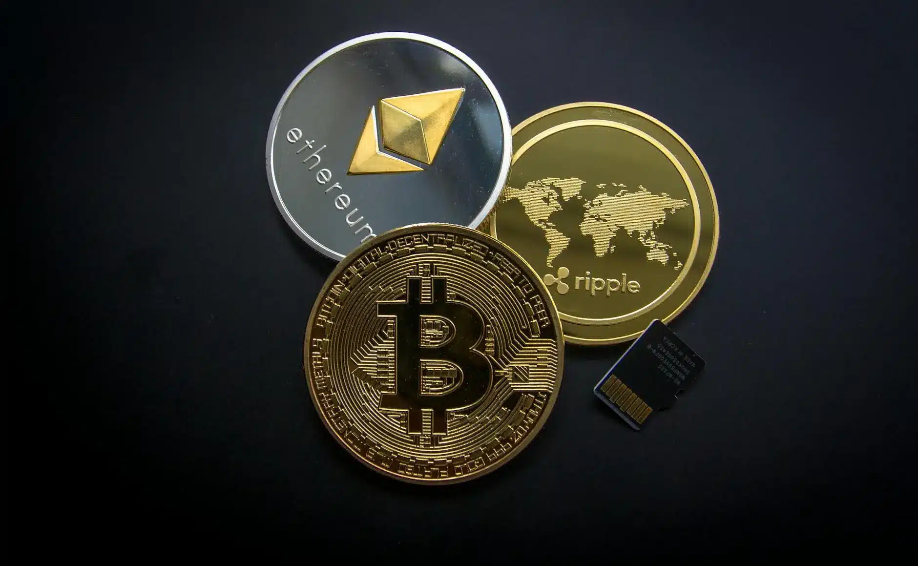 Three cryptocurrency coins: Bitcoin, Ethereum, and Ripple, with a microSD card.