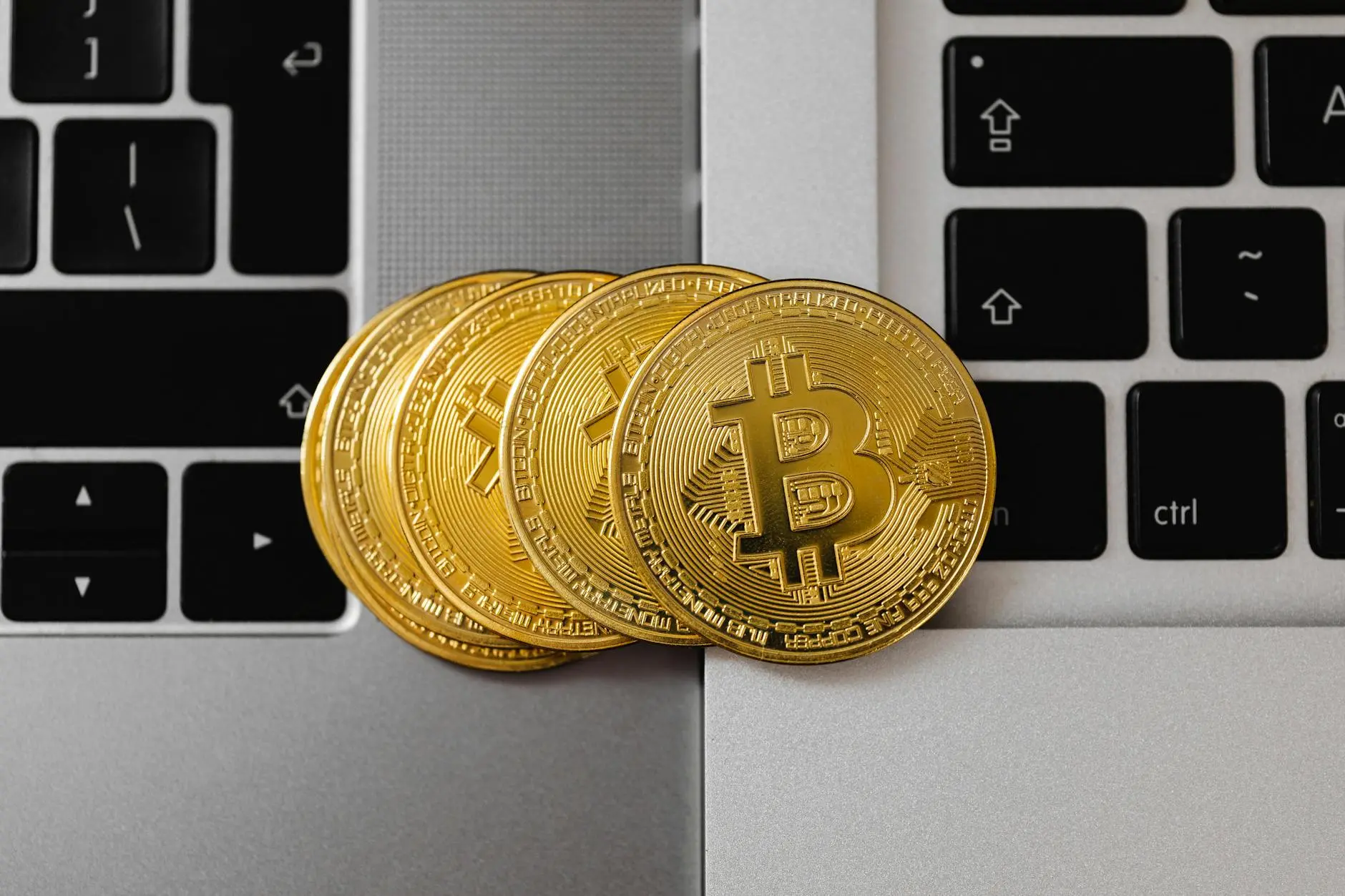 Four gold Bitcoin coins on laptop keyboards.