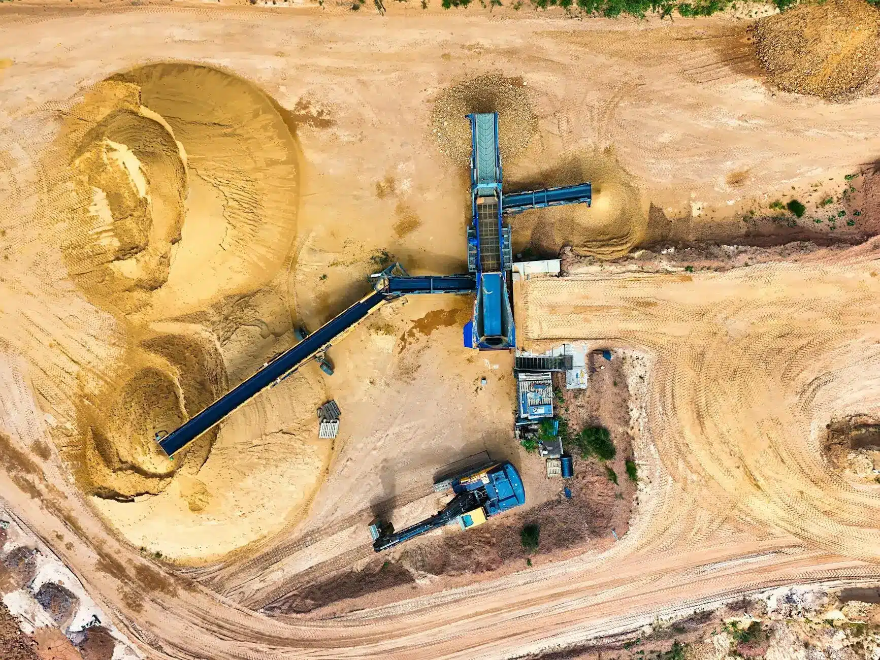 Aerial view of a mining operation with heavy machinery and sand piles.