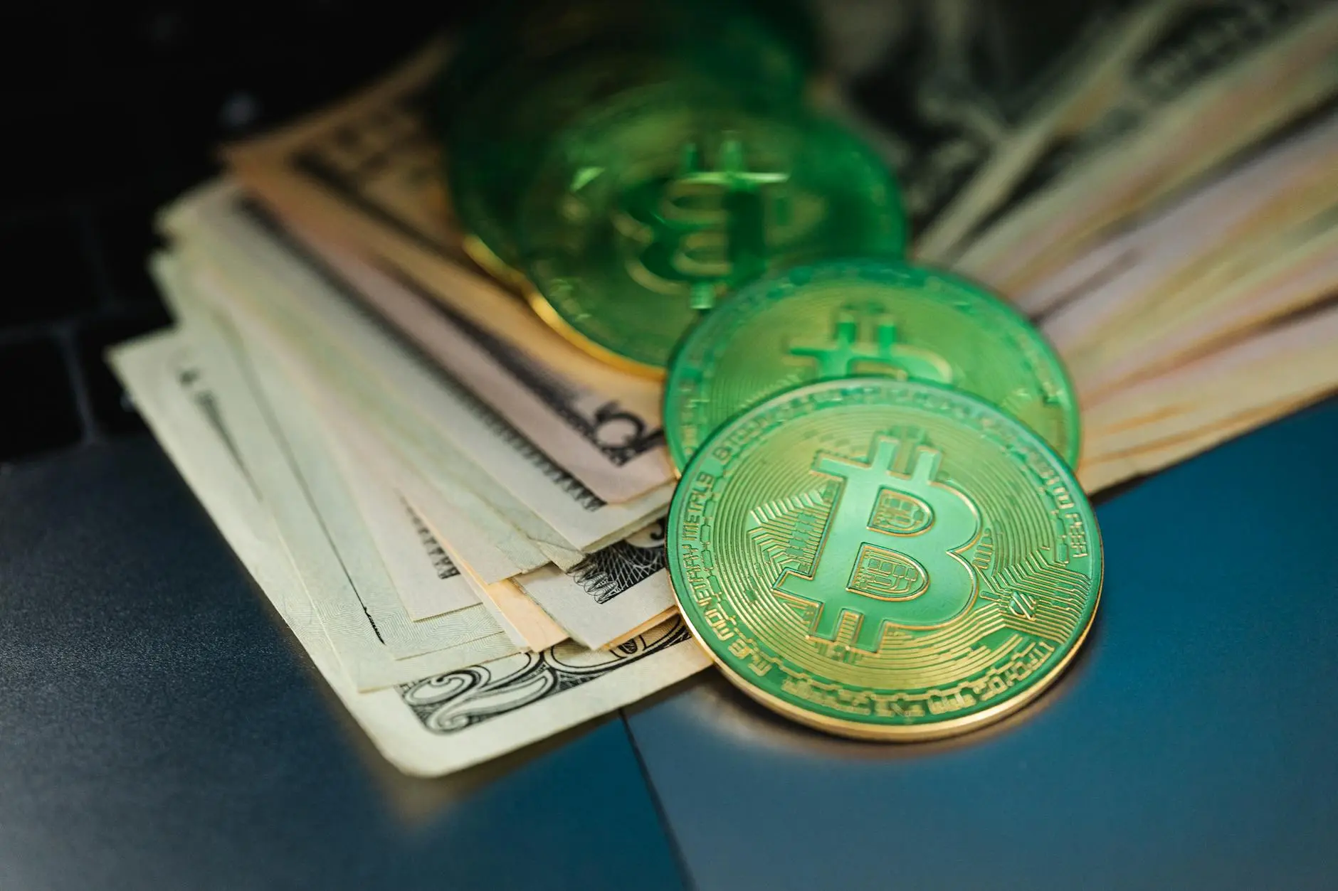 Stack of cash with shiny Bitcoin coins on a dark surface.