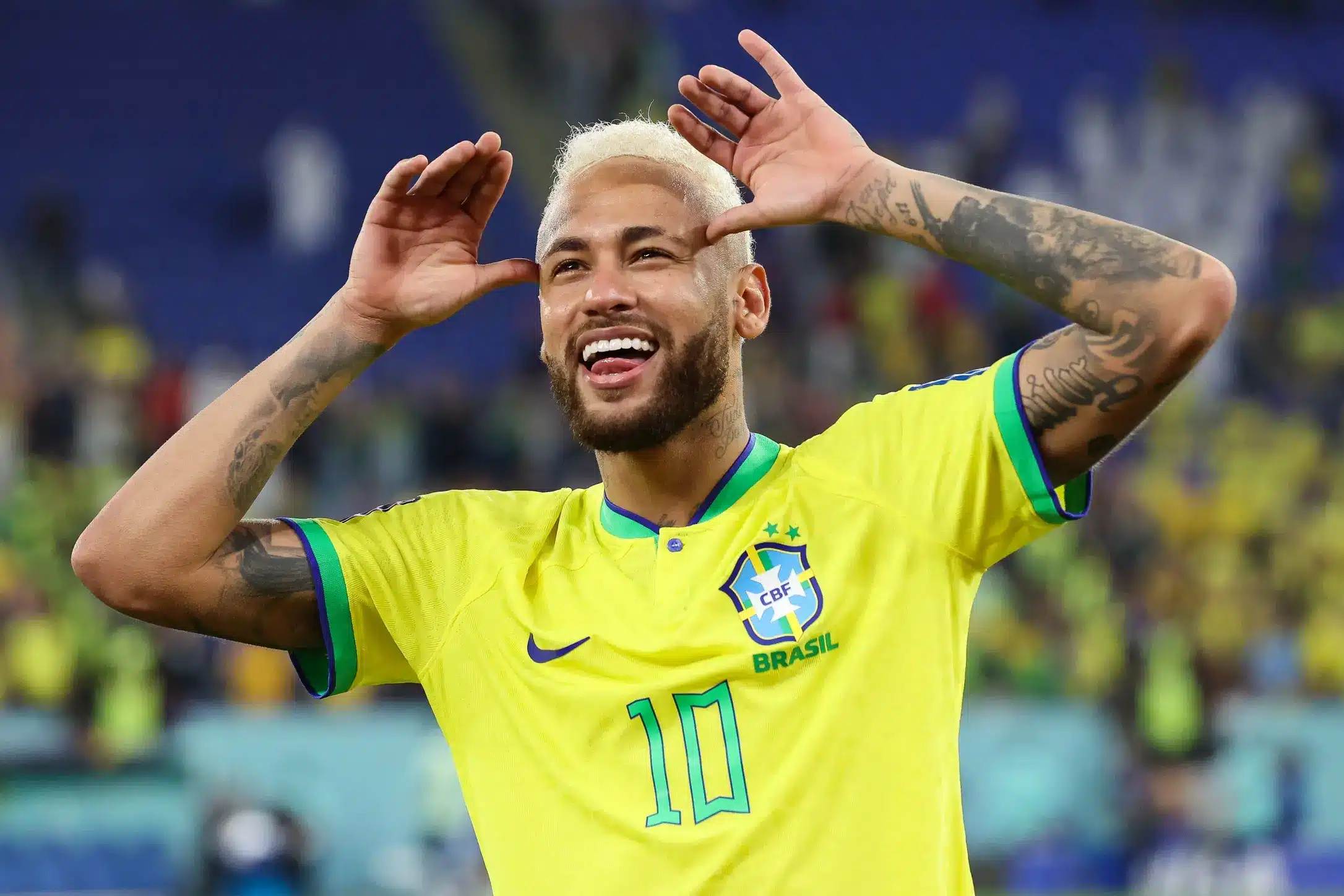 A joyful soccer player in a yellow Brazil jersey celebrates with a big smile.