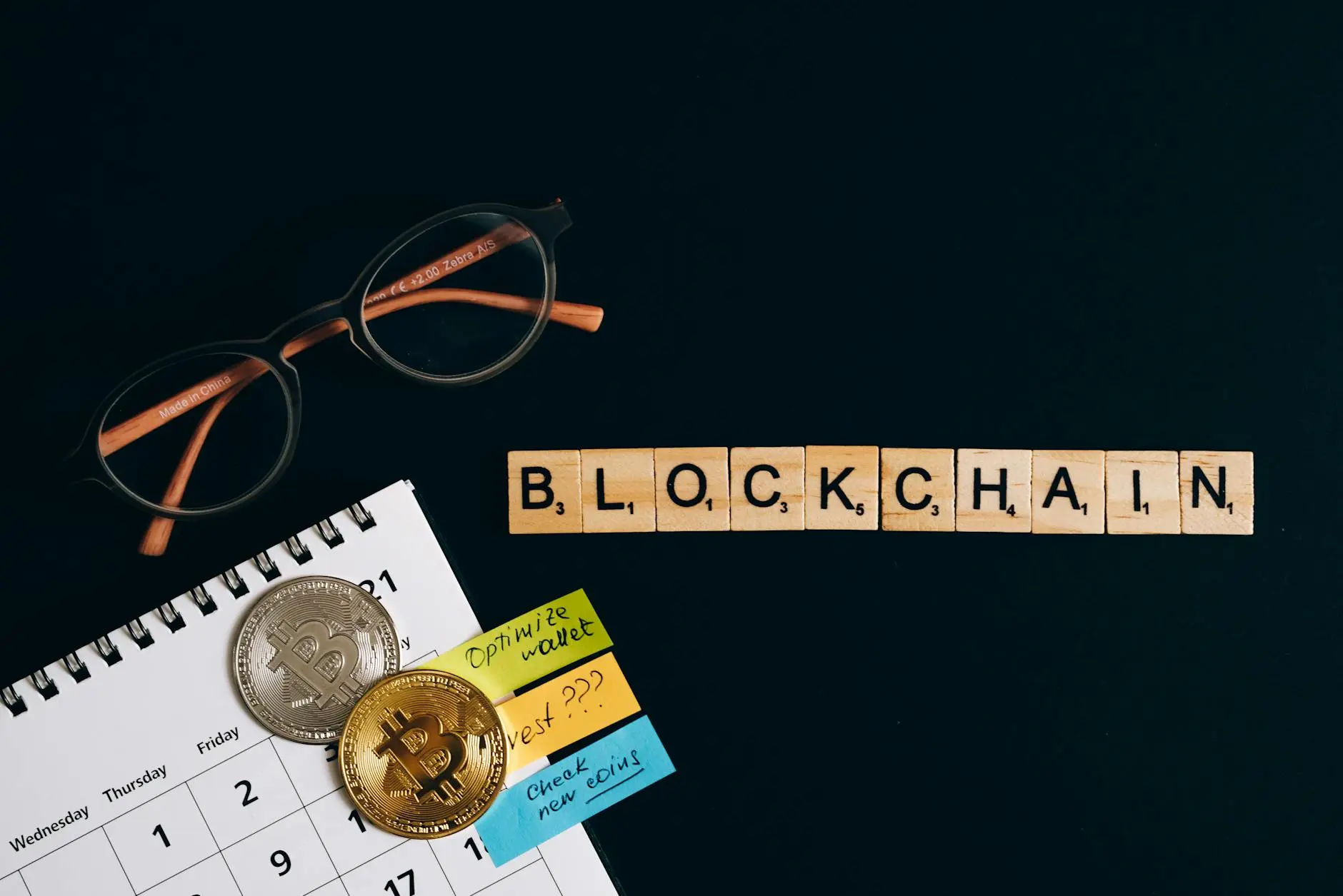 Scrabble letters spelling 'BLOCKCHAIN' with glasses and Bitcoin coins on a calendar.