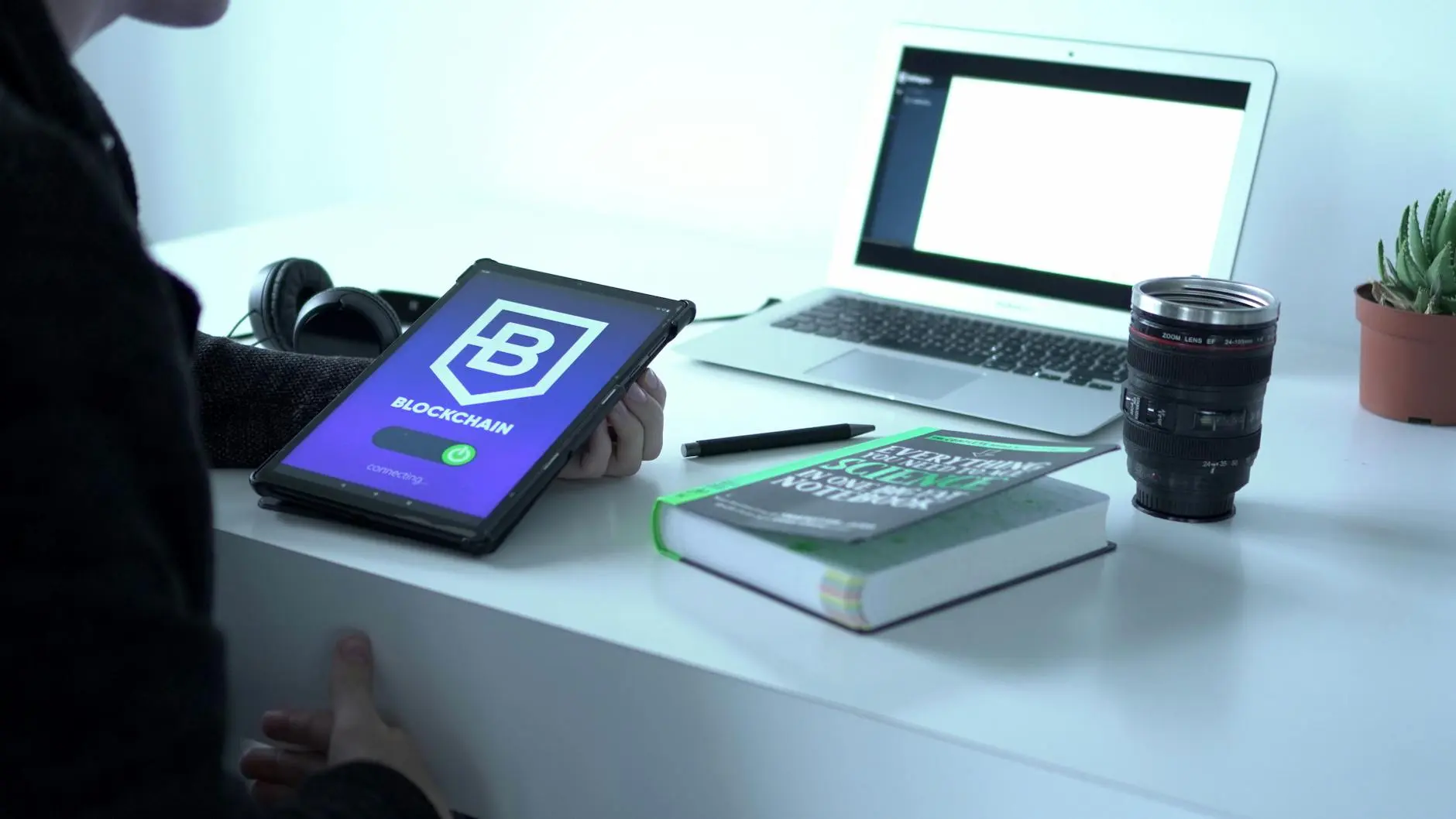 A person holding a tablet displaying a blockchain app in a modern workspace.