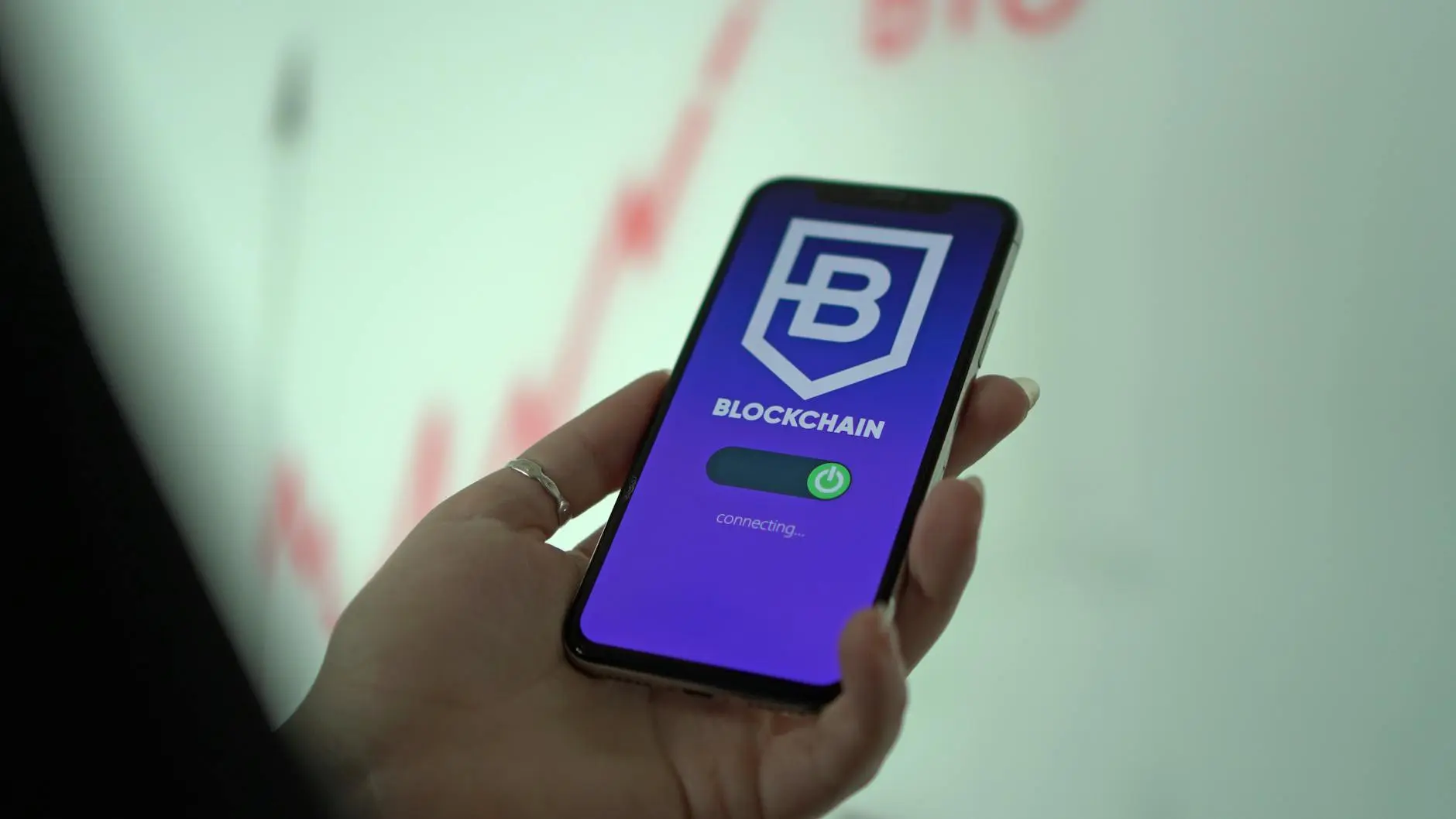 A hand holding a phone displaying a blockchain app interface.