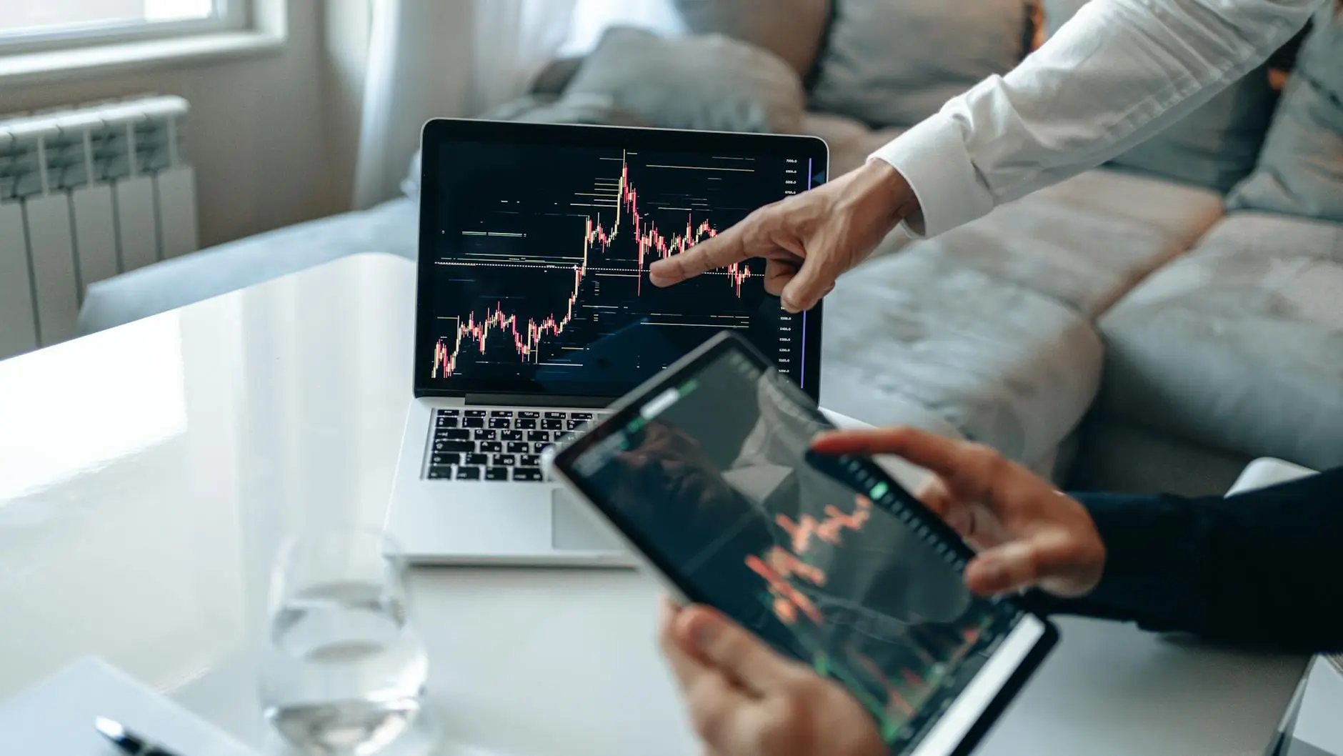 Two people analyzing financial market graphs on a laptop and tablet.