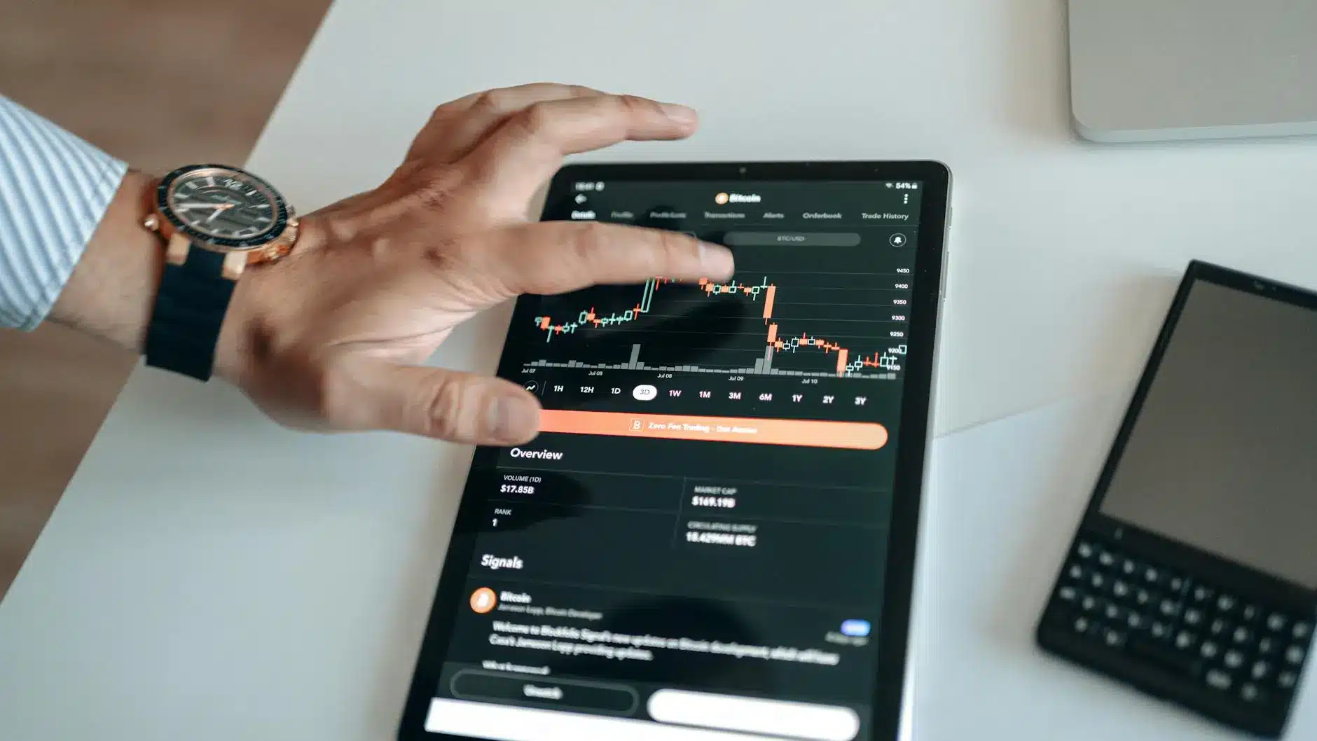 Person analyzing a bitcoin price chart on a tablet, with a smartphone nearby.