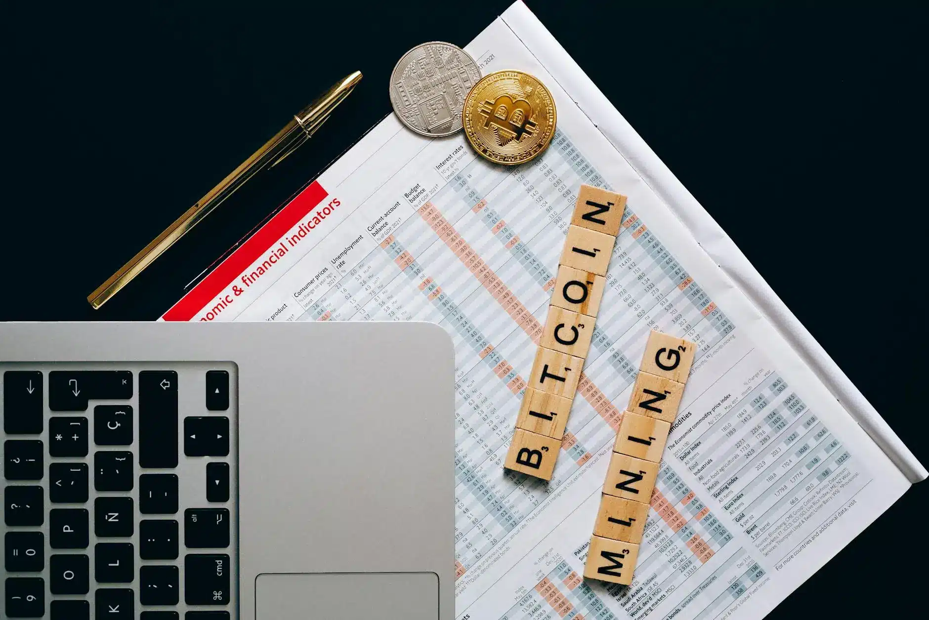 Top view of a laptop, cryptocurrency coins, and Scrabble tiles spelling 'BITCOIN MINING'.
