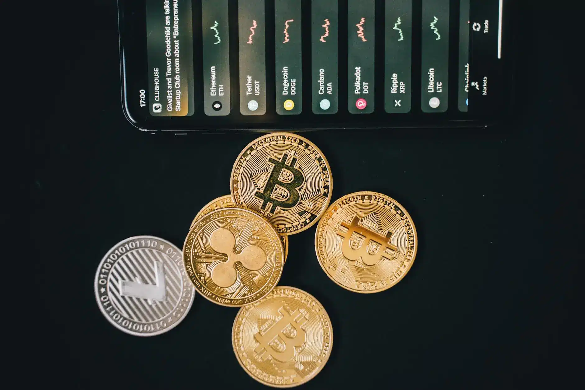 A smartphone displaying cryptocurrency prices next to gold and silver coins.