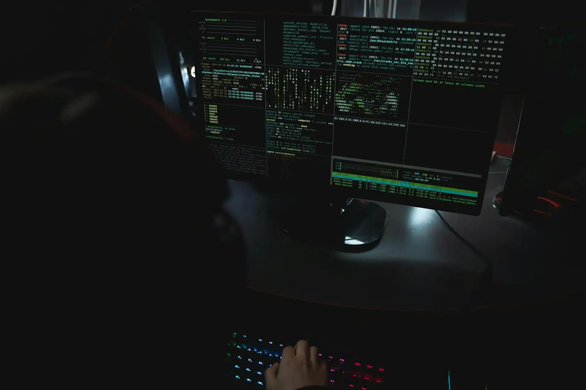 Dark computer setup displaying code and command lines on multiple screens.