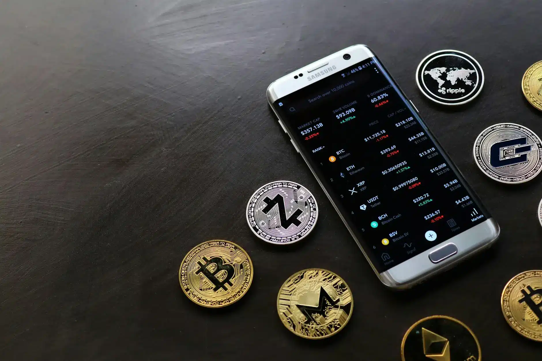Smartphone displaying cryptocurrency market data next to various coins.