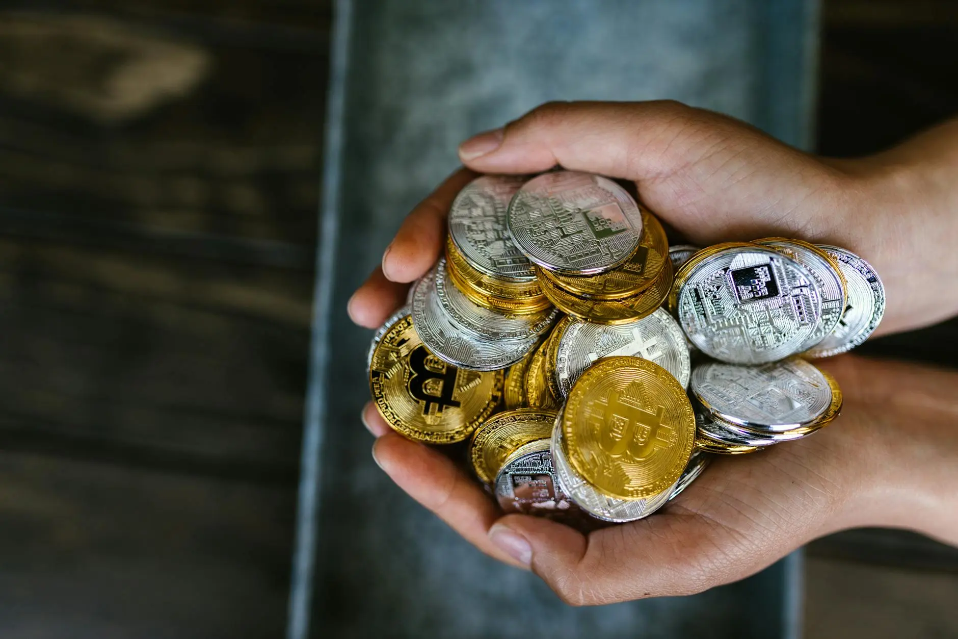 Hands holding a variety of cryptocurrency coins, including Bitcoin in gold and silver.