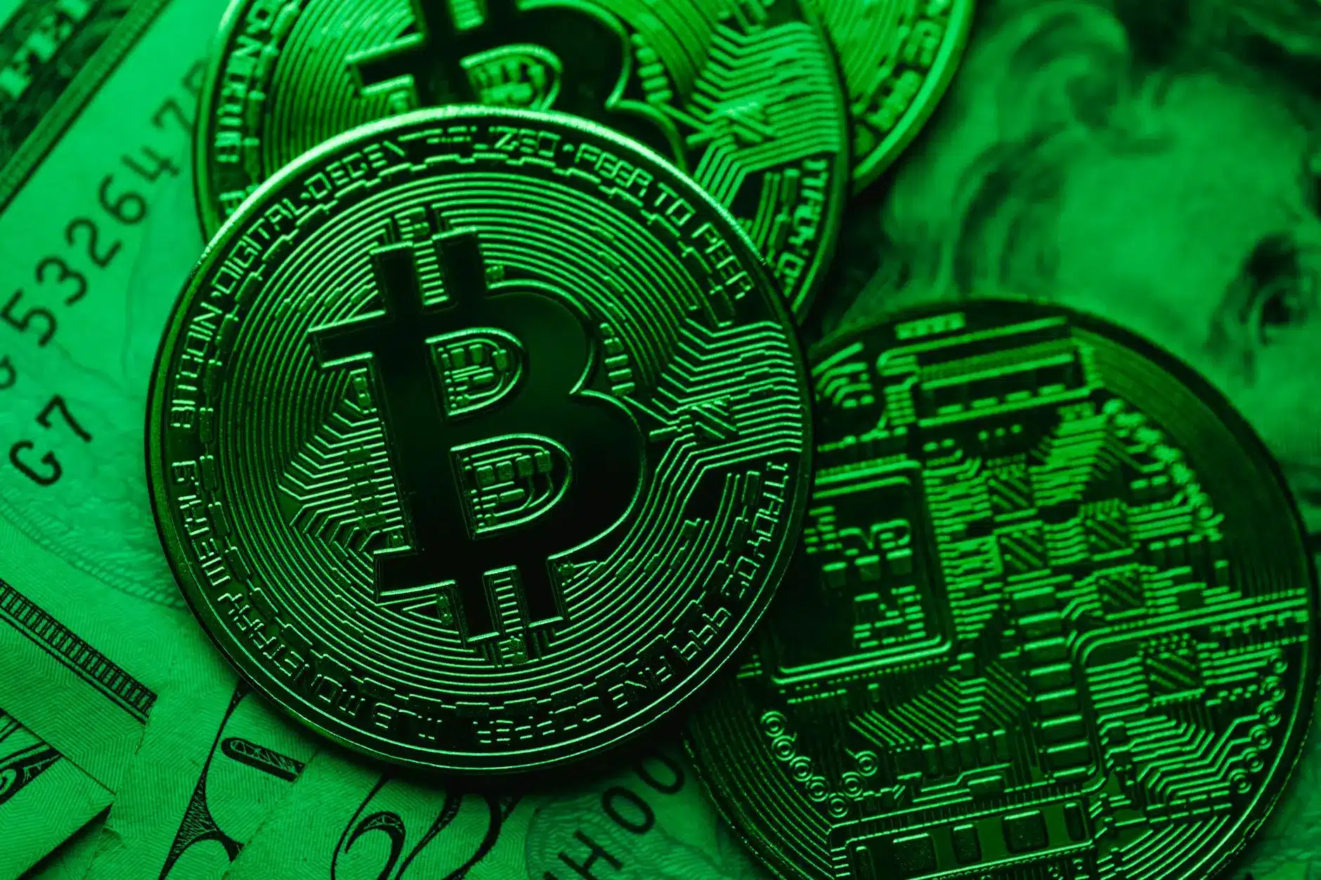 Close-up of Bitcoin coins against a green backdrop and dollar bills.