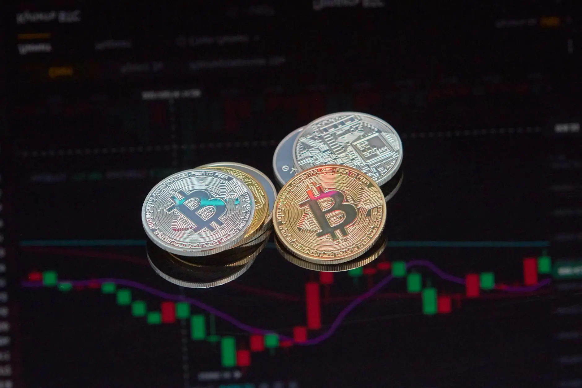 Three Bitcoin coins on a reflective surface with a trading chart background.