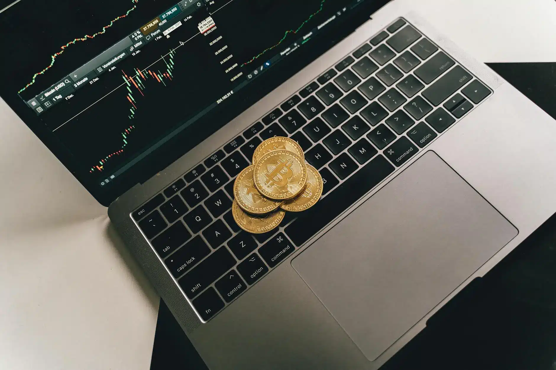 A laptop keyboard with Bitcoin coins and a trading chart on screen.