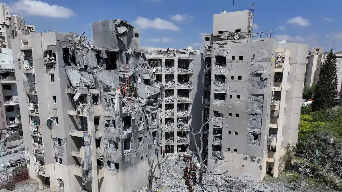 Damaged multi-story building with debris and exposed interiors after airstrikes.