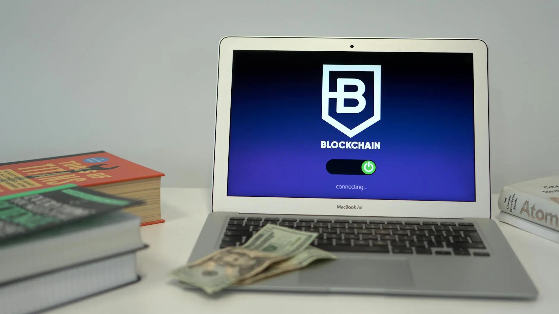 A laptop displaying a blockchain login screen, with books and cash nearby.