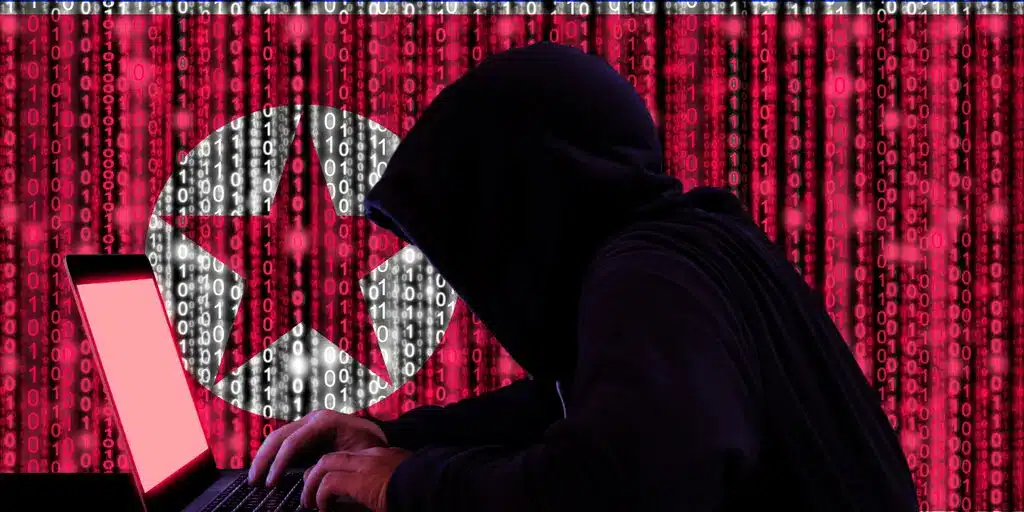 Hooded figure typing on a laptop with binary code and North Korean flag background.
