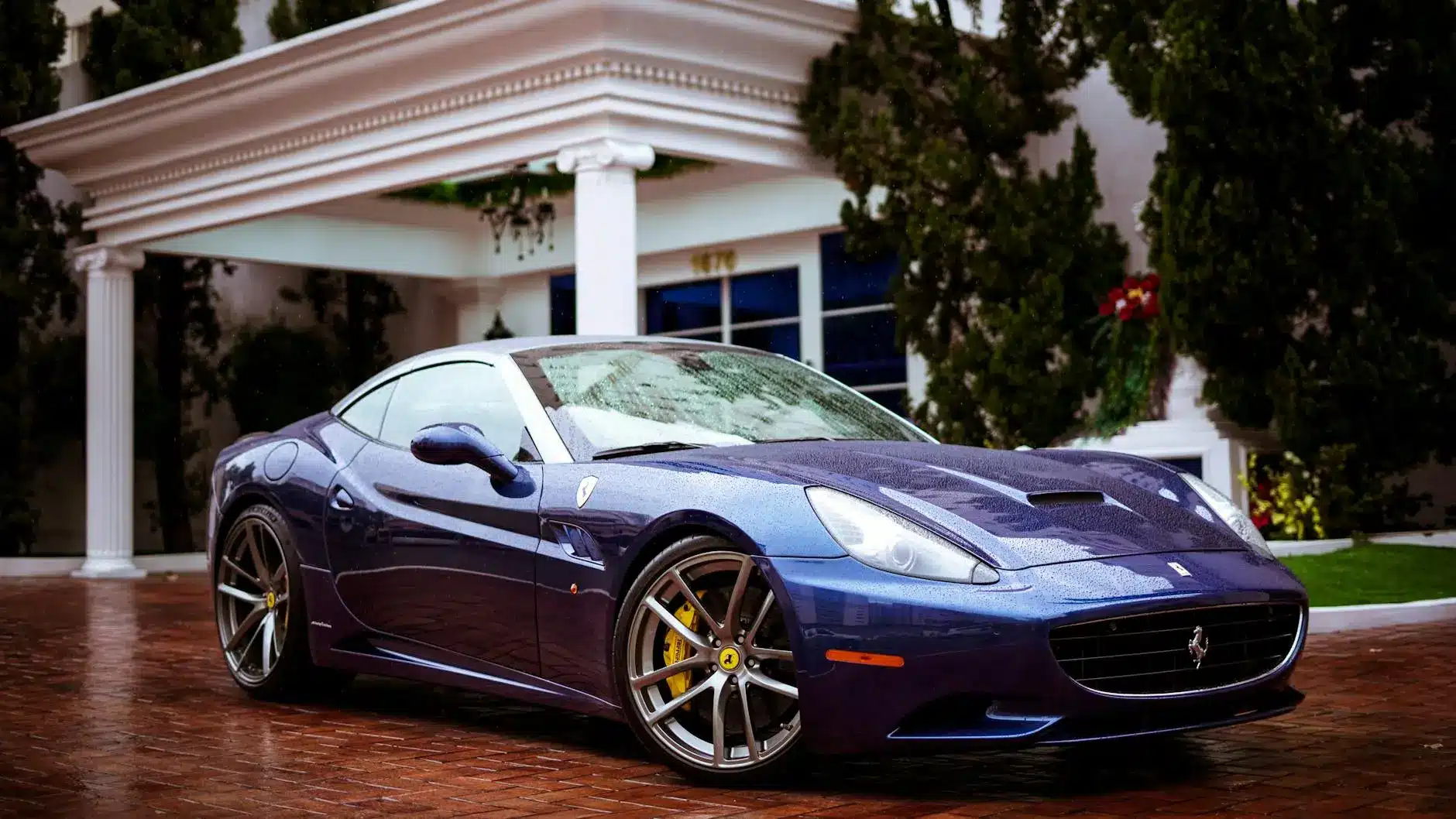 A luxury purple Ferrari parked on a brick driveway in front of a mansion.