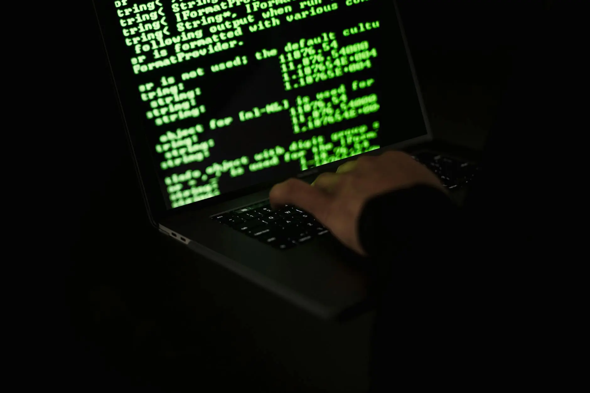 Close-up of a hand typing on a laptop displaying code in green text