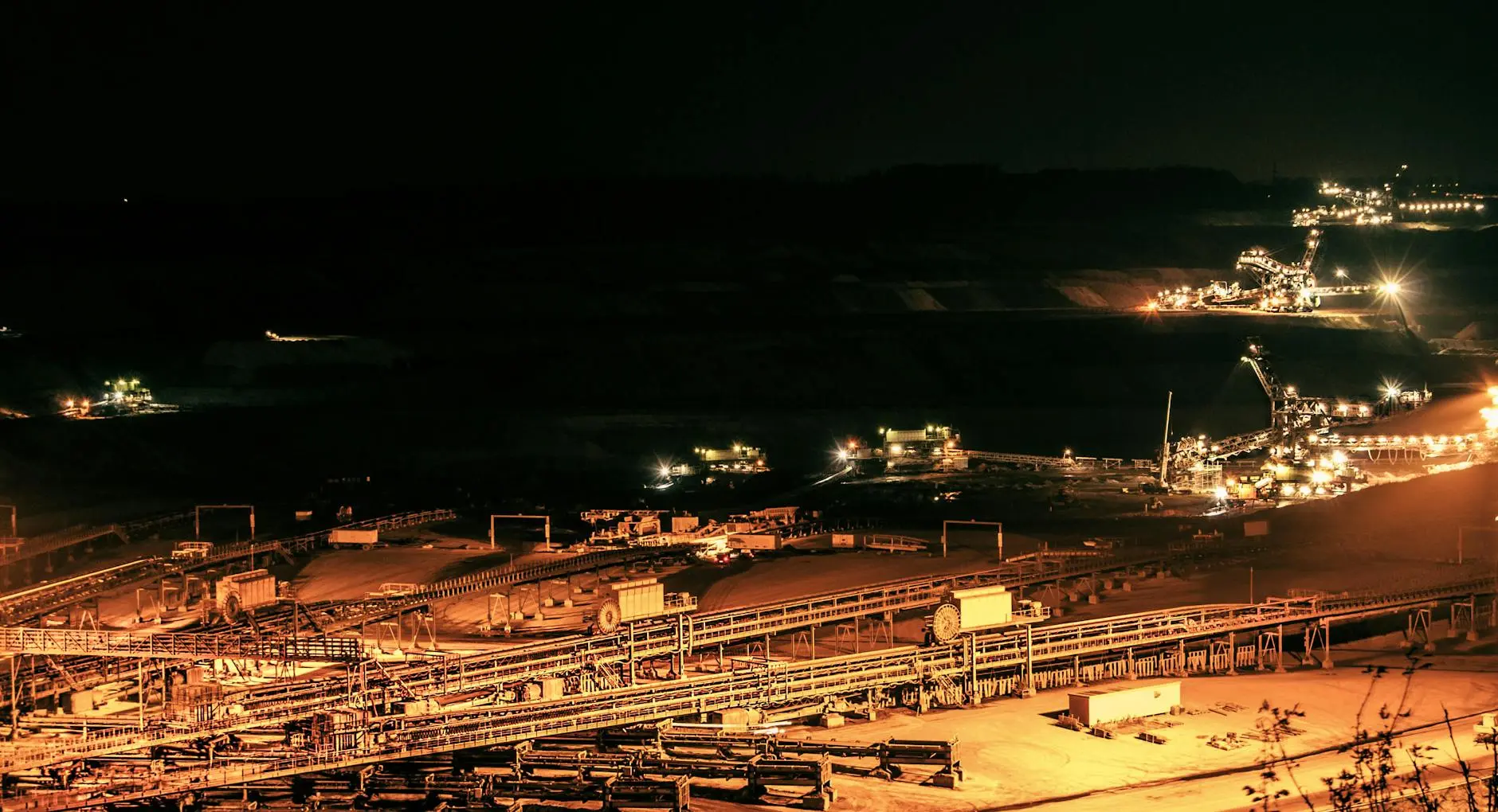 Night view of mining operations with illuminated machinery and conveyor belts.