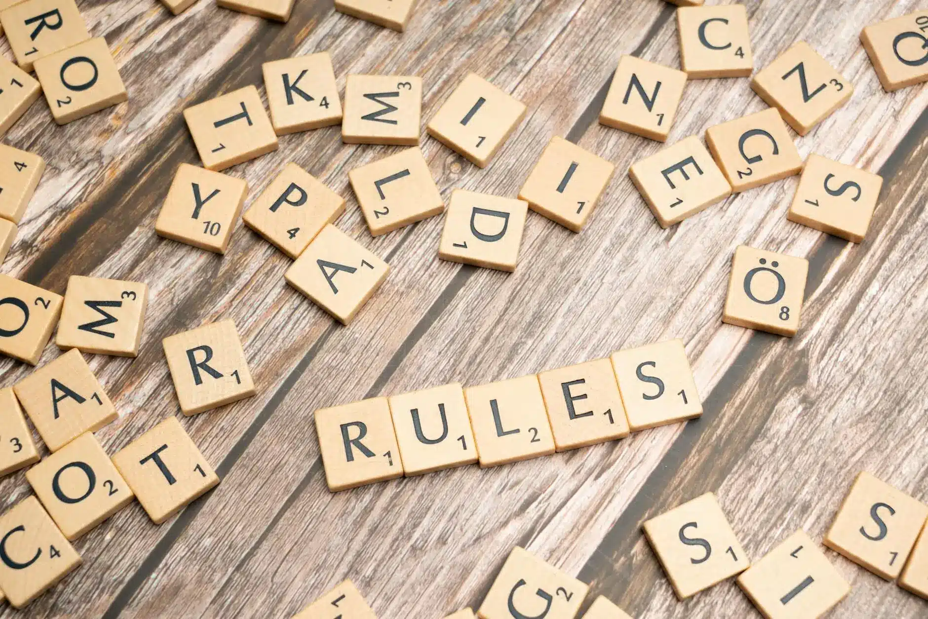 Scrabble tiles scattered on a wooden surface, forming the word 'RULES'.