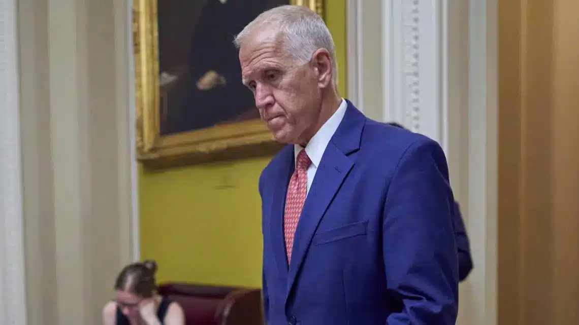 Senator Thom Tillis in a blue suit with a serious expression, standing in a legislative chamber.