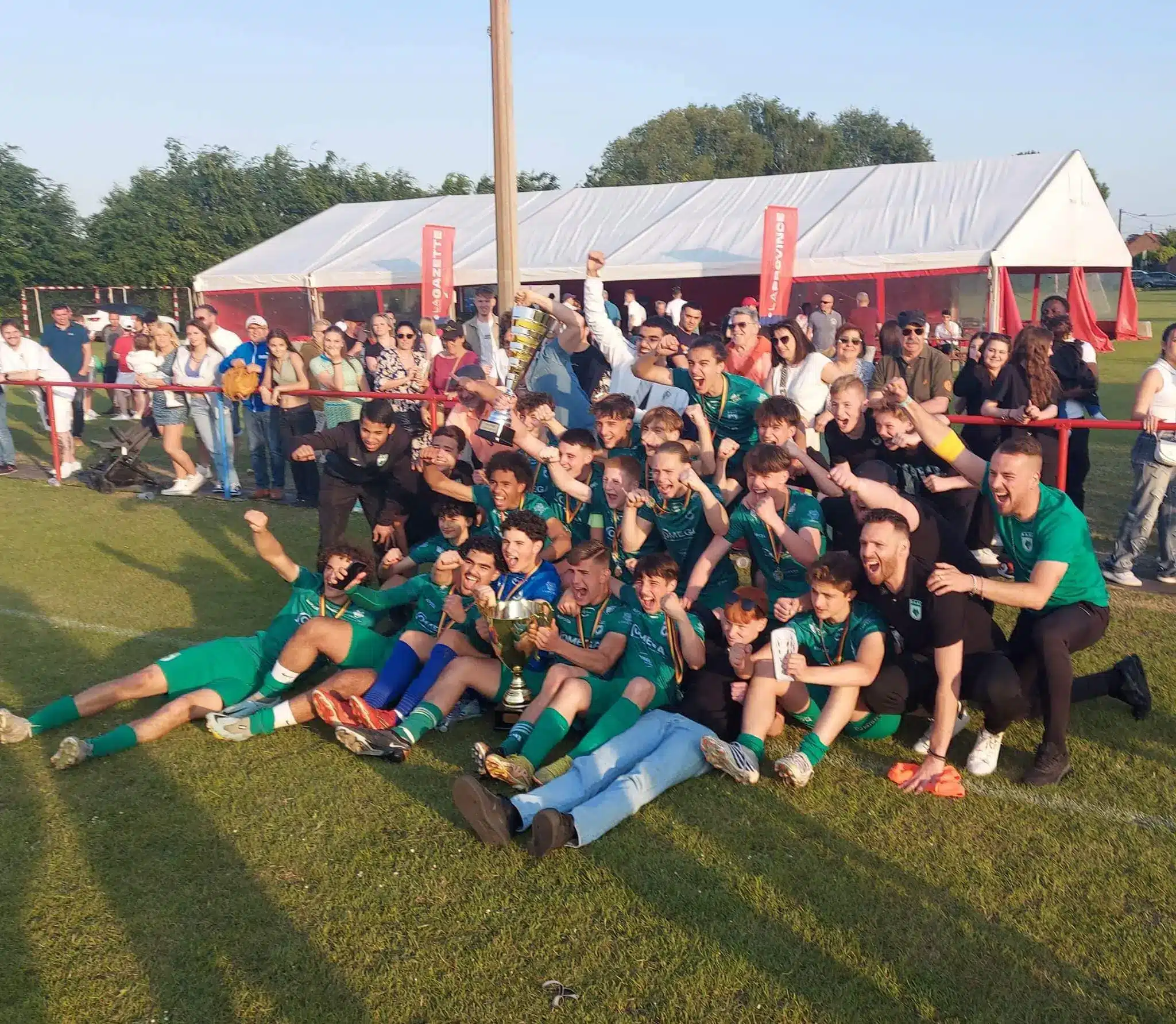 Youth soccer team celebrating with a trophy on a field surrounded by fans.