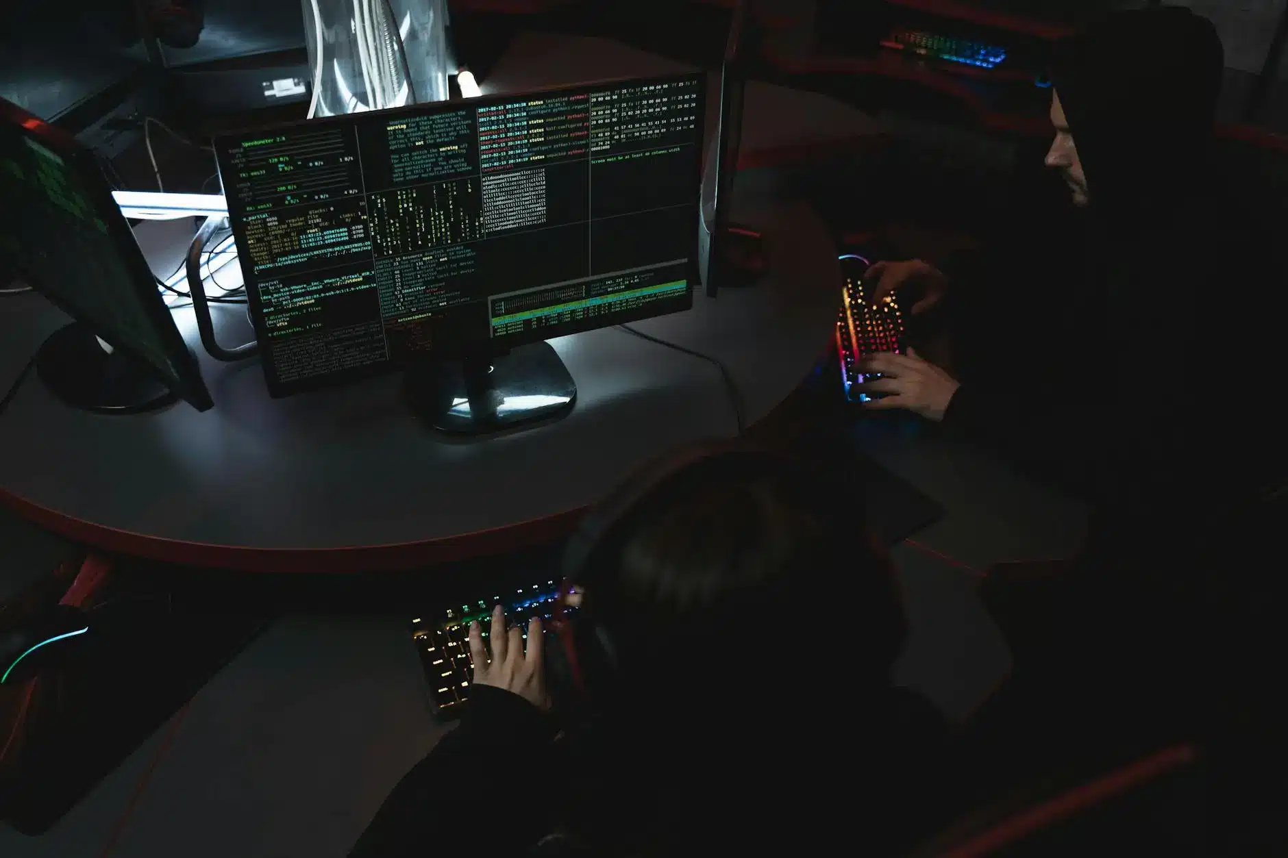 Two individuals working at computers with code and data displayed on screens.