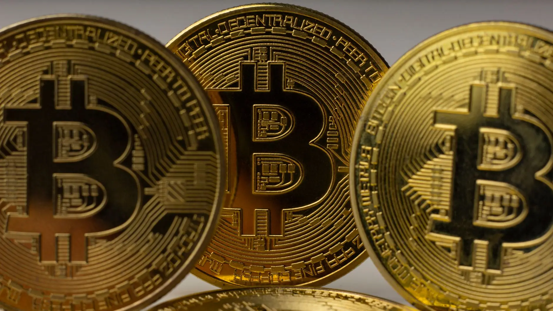 Three gold Bitcoin coins displayed closely together against a neutral background.