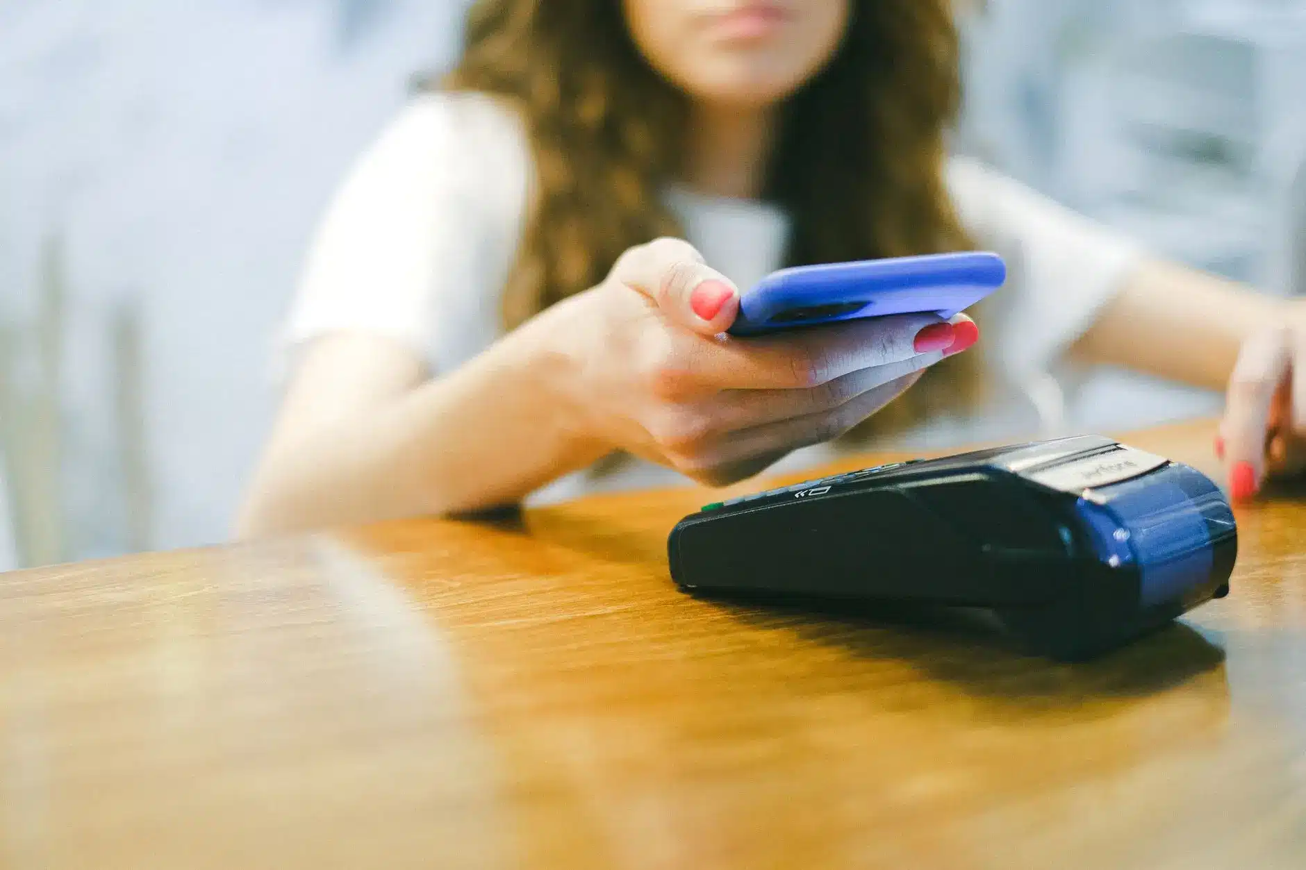 A woman using a smartphone for contactless payment at a card reader.