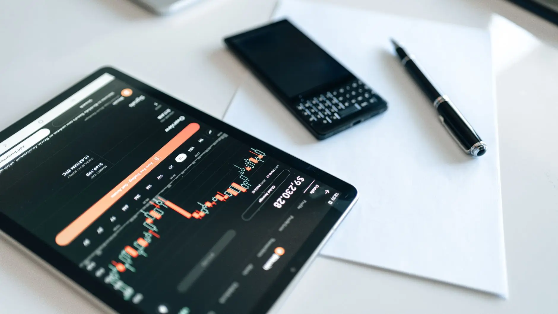 Close-up of a tablet displaying cryptocurrency charts alongside a smartphone and pen.