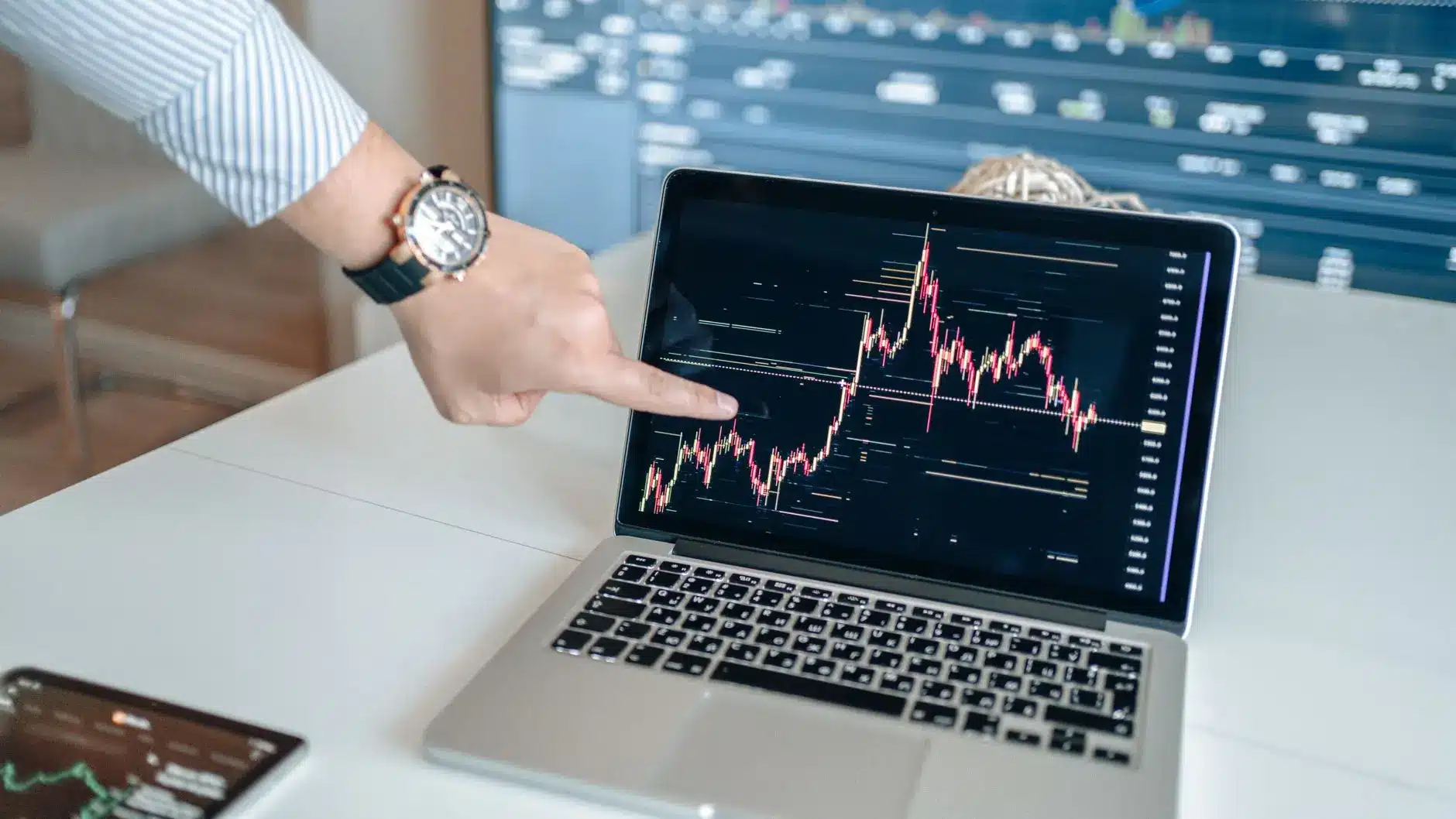 Trader analyzing a financial chart on a laptop screen in an office setting.