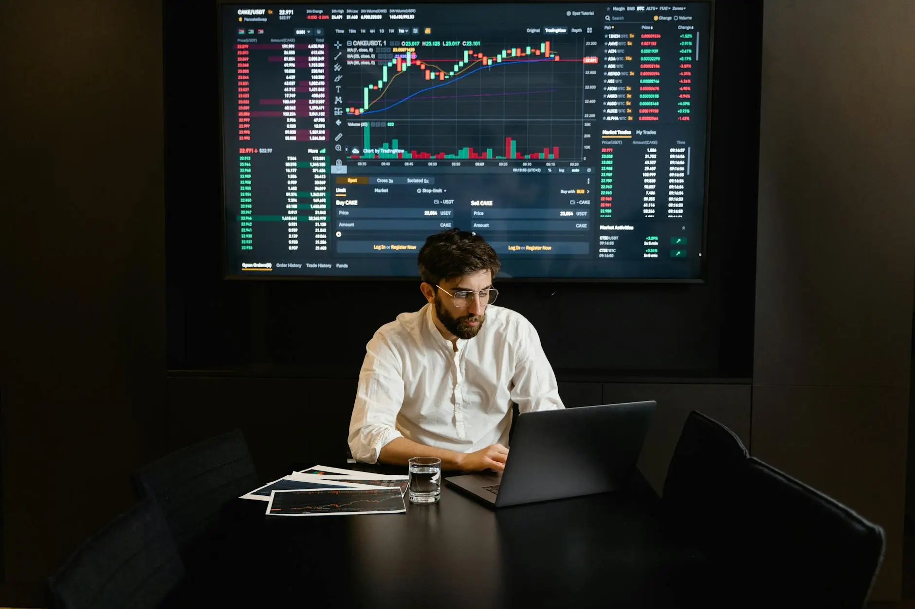 A trader analyzing cryptocurrency data on a laptop with charts displayed on a screen.