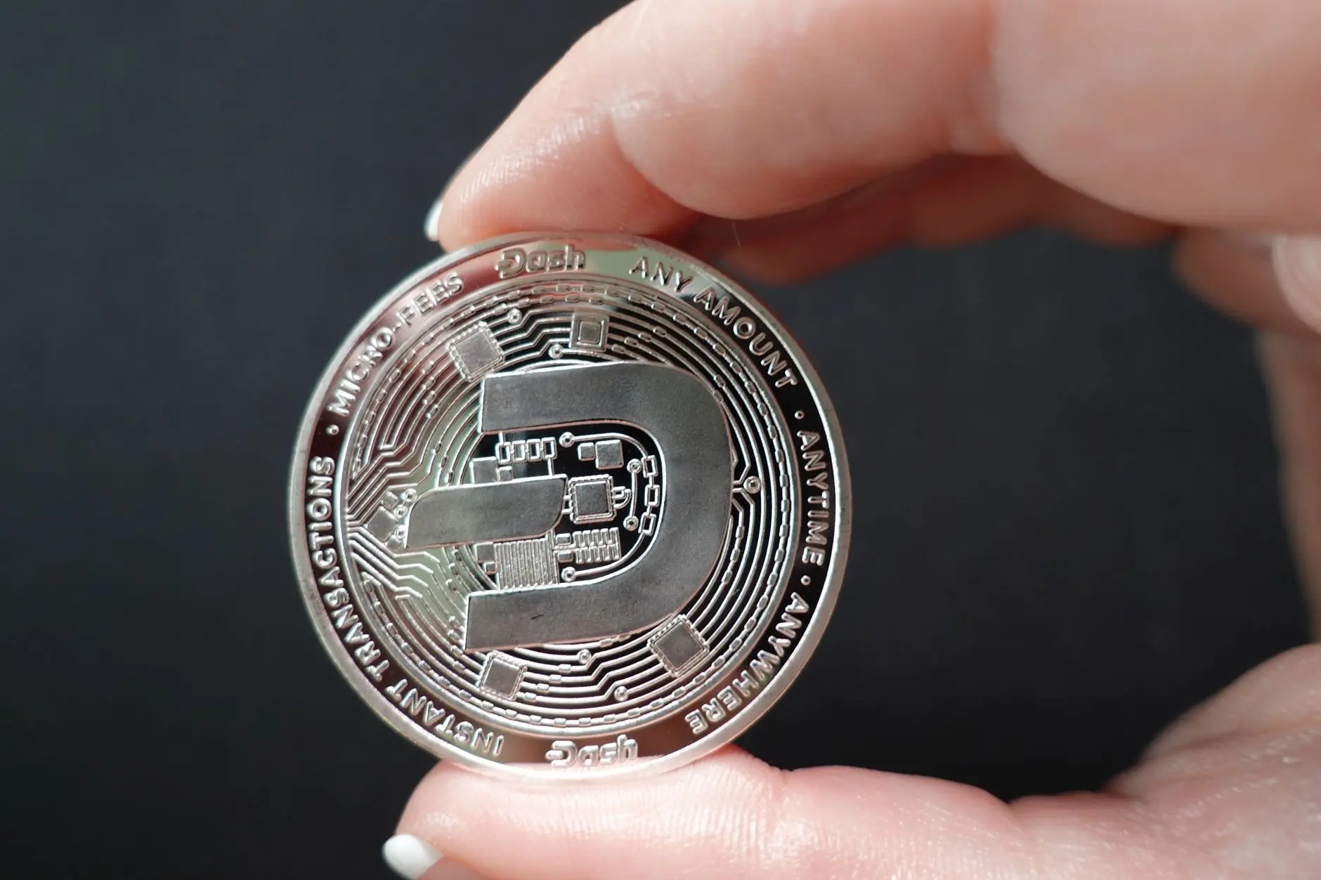 Close-up of a hand holding a Dash cryptocurrency coin.