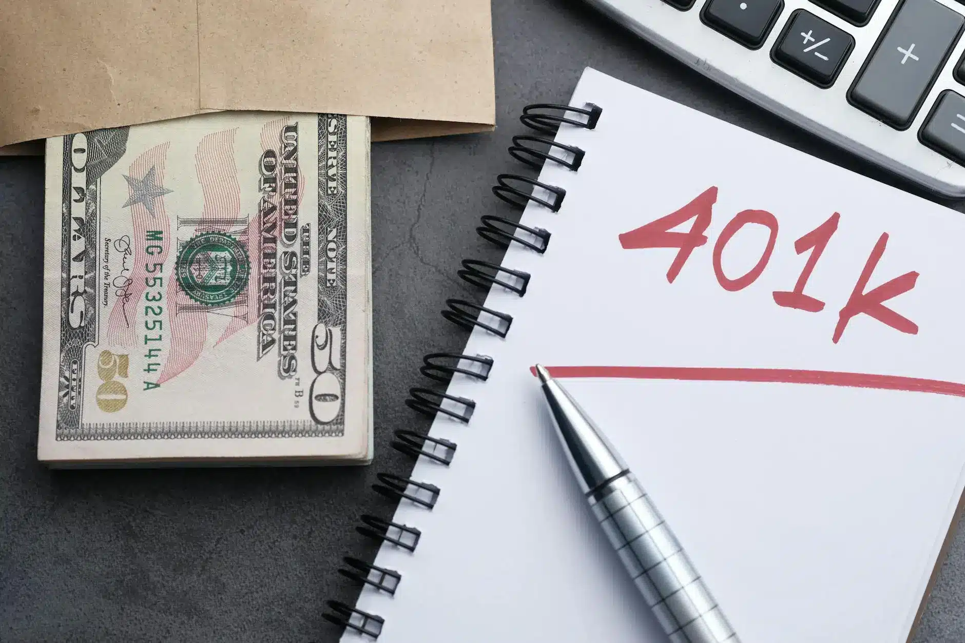 A stack of cash in an envelope next to a notebook with '401k' written on it.